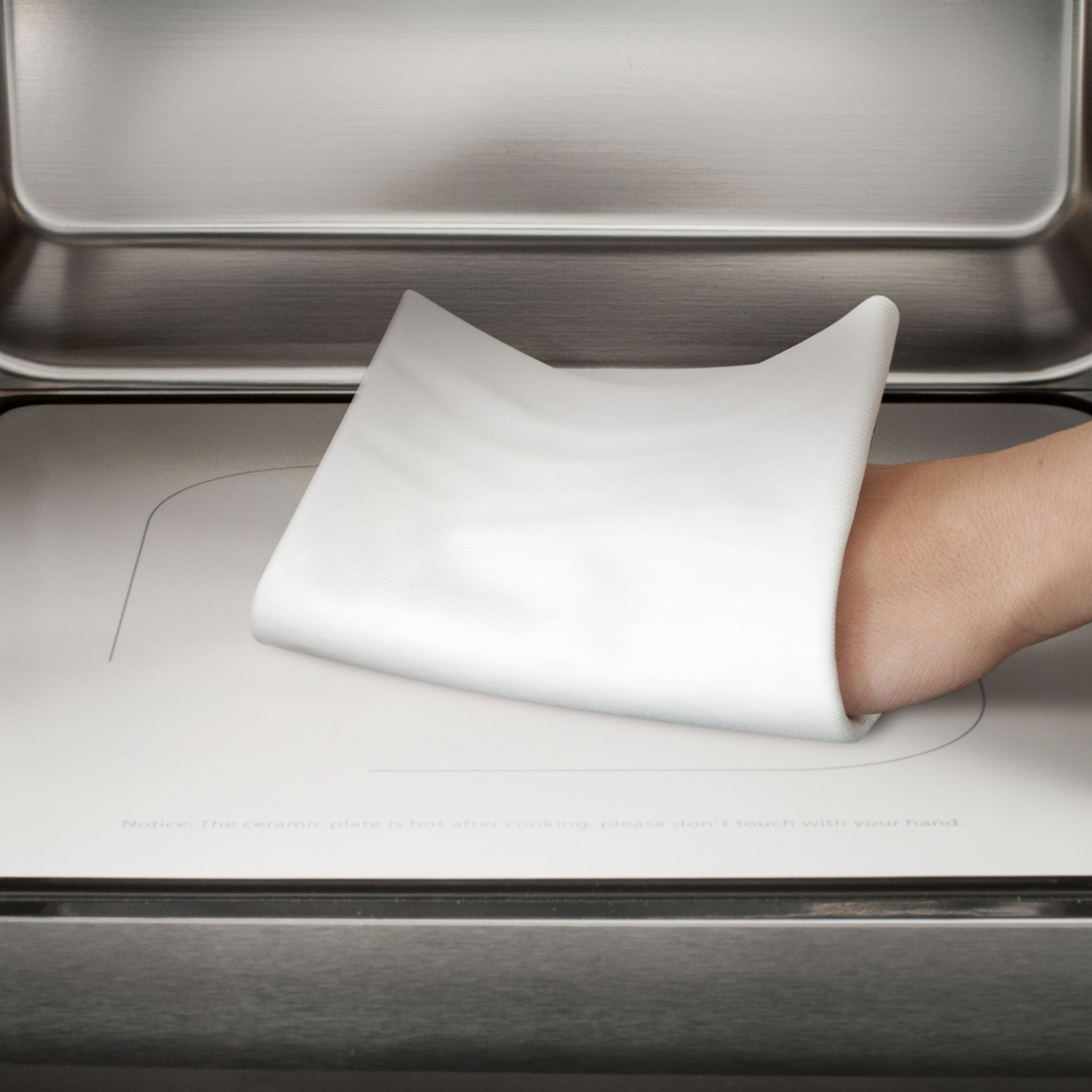 Una mano che posiziona una piastra in ceramica bianca in un forno in acciaio inossidabile. Avviso: caldo dopo la cottura.