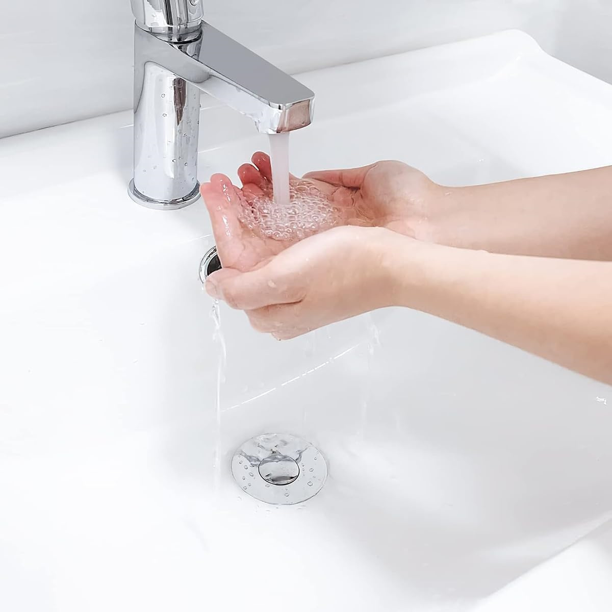 Hände unter fließendem Wasser, waschen sich in einem weißen Waschbecken, mit einem Chromhahn darüber.