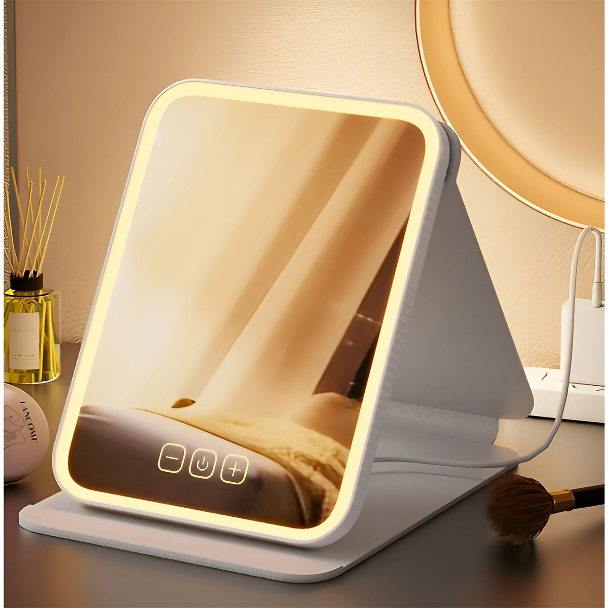 Ein beleuchteter Schminkspiegel mit Touch-Bedienelementen und einem Pinsel. Der Spiegel spiegelt ein Bett wider.