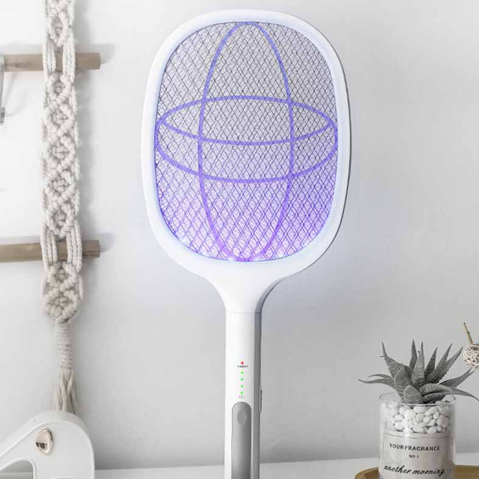 Weißer elektrischer Fliegenfänger mit violettem Licht. Hängt an einer Wand mit Makramee-Dekoration.