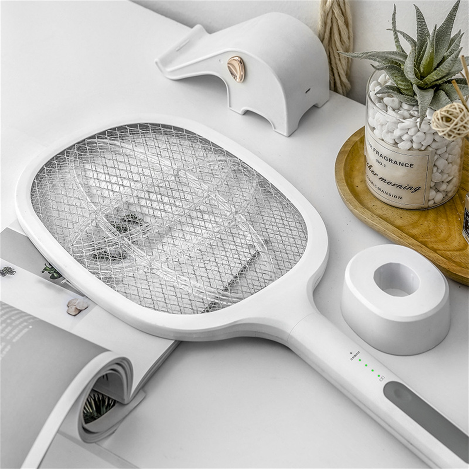 Ein weißer elektrischer Fliegenfänger und Ständer auf einem Tisch, mit einer Pflanze und einer dekorativen Elefantenfigur.