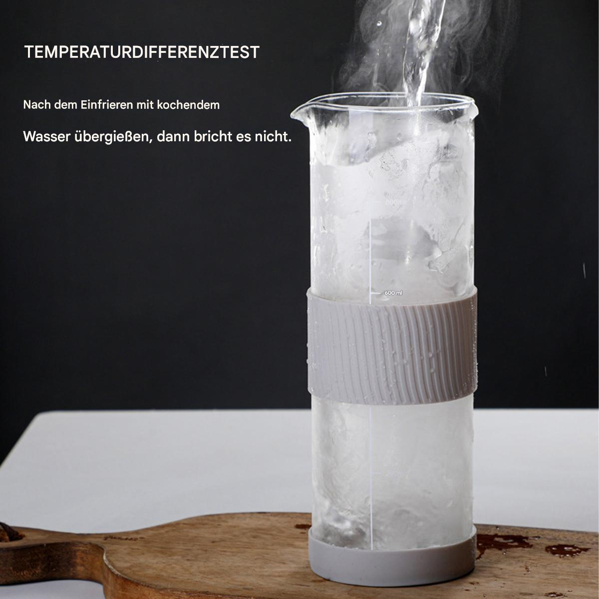 Glaszylinder mit Eis und Wasser. Heißes Wasser wird eingegossen, neben Holzbrett.