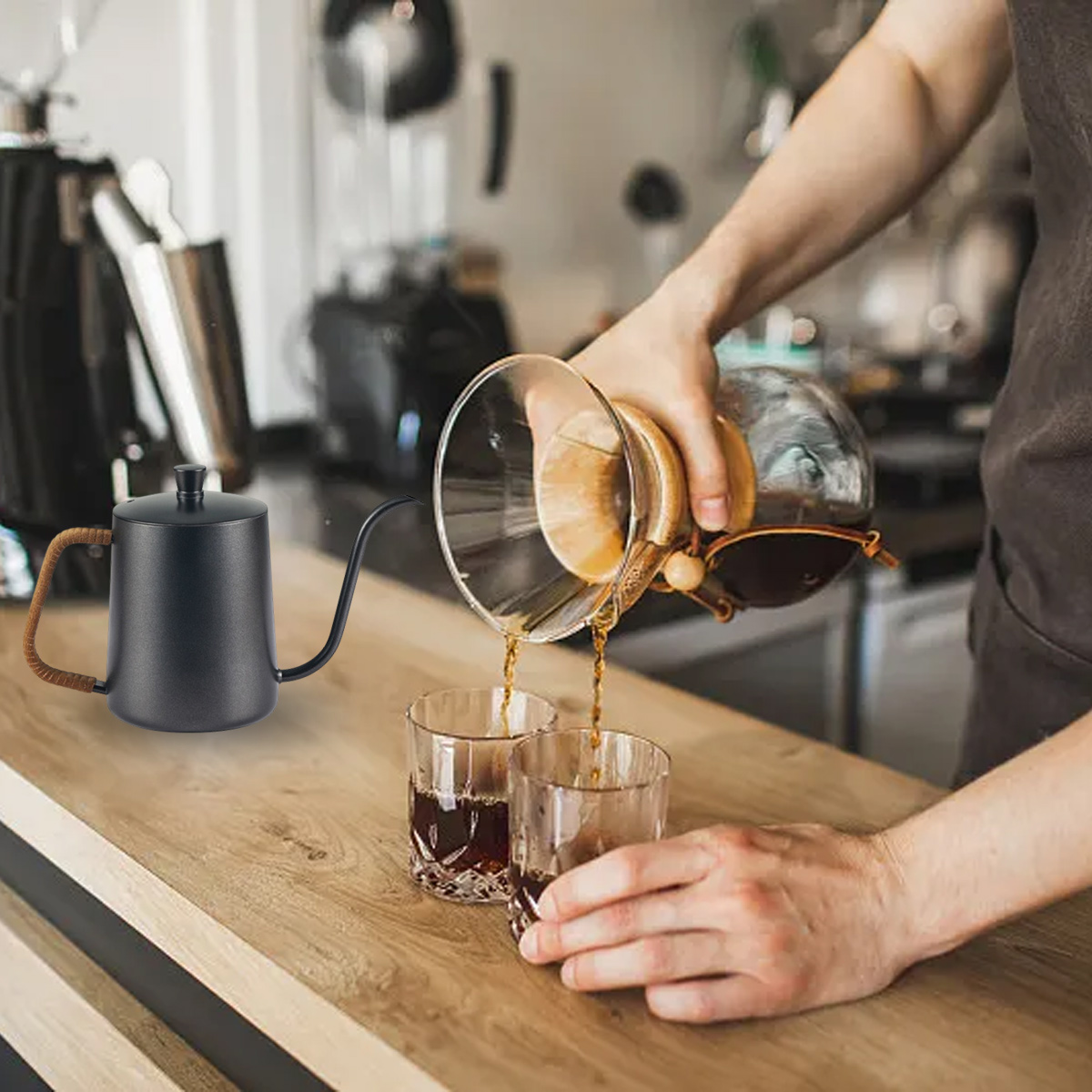 Eine Person gießt Kaffee aus einem schwarzen Kessel in zwei Gläser auf einer Holzoberfläche.