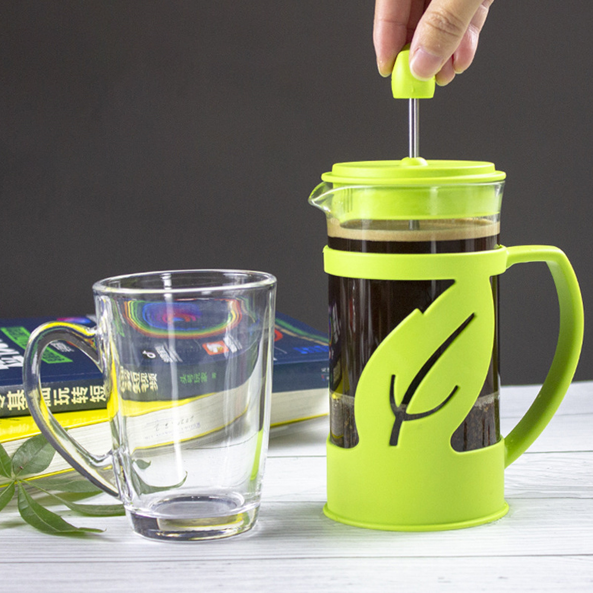 French Press mit grünen Akzenten. Glas und grüner Halter. Kaffeetasse. Hand hält die Presse.