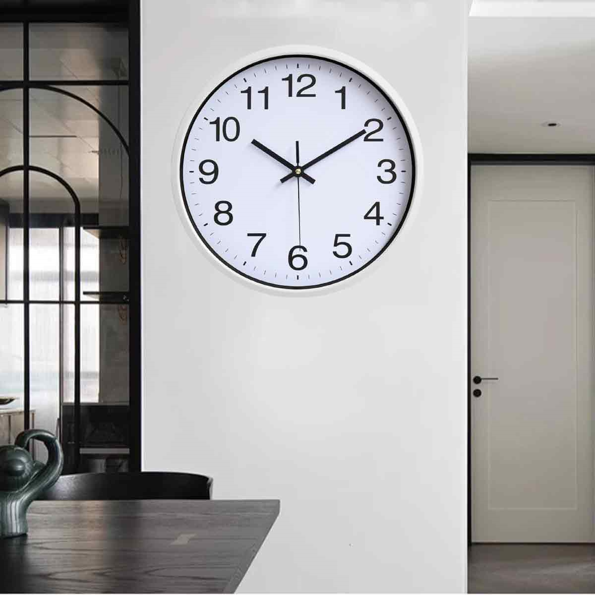 Weiße Wanduhr mit schwarzen Zahlen und Zeigern. Schwarzer Rahmen. Weiße Wand, Inneneinstellung.