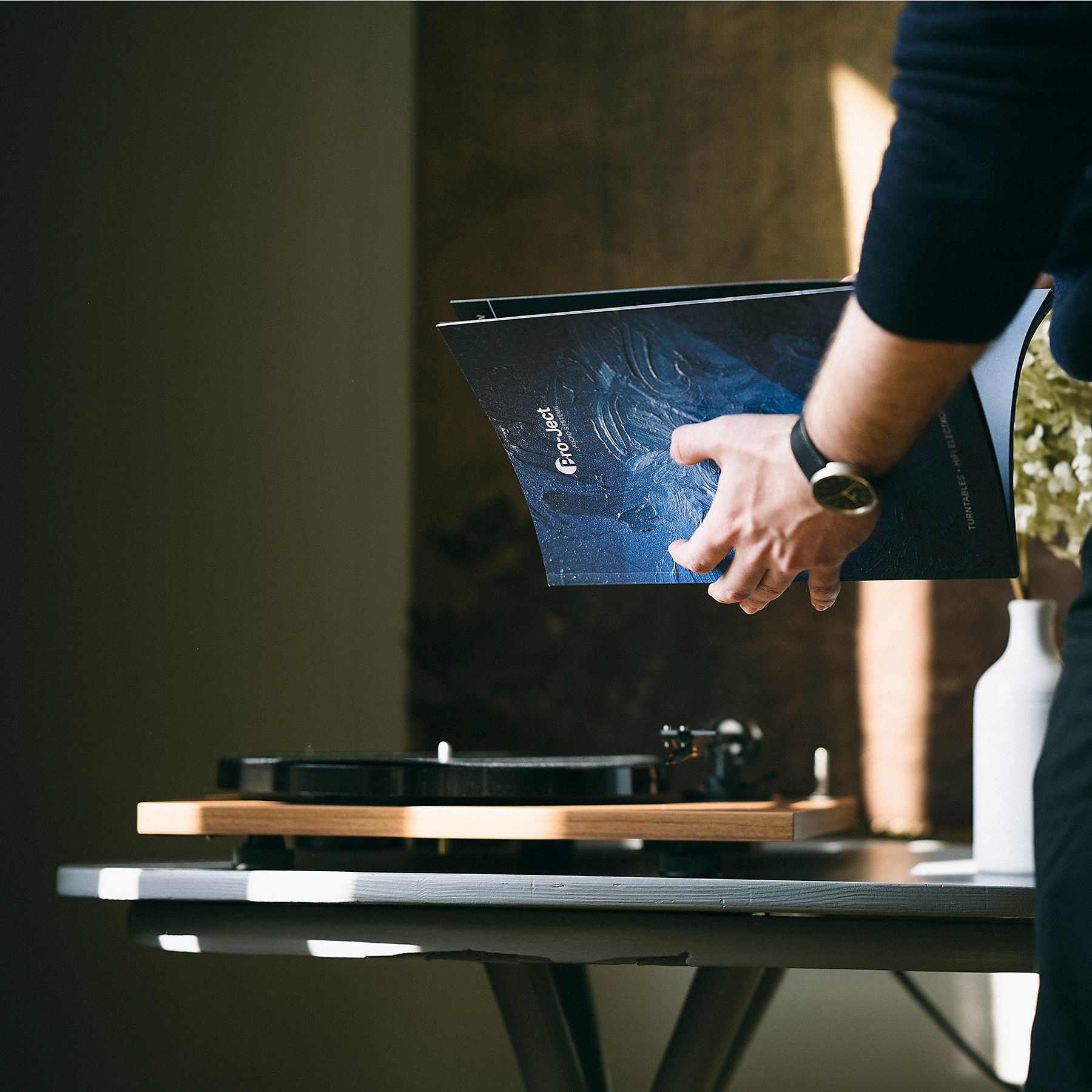 Osoba trzymająca płytę winylową w pobliżu gramofonu na stole.