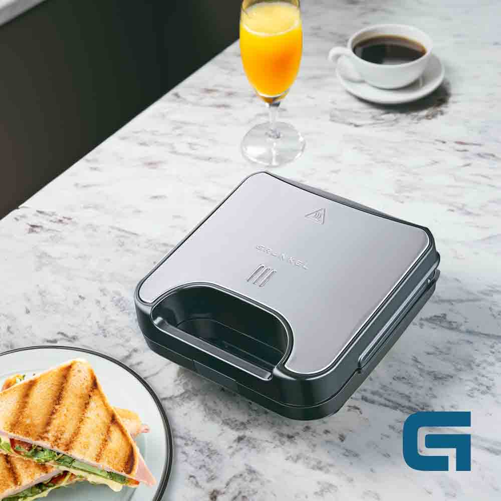 Un tostapane per sandwich con un sandwich e una bevanda su un tavolo, con un logo G.