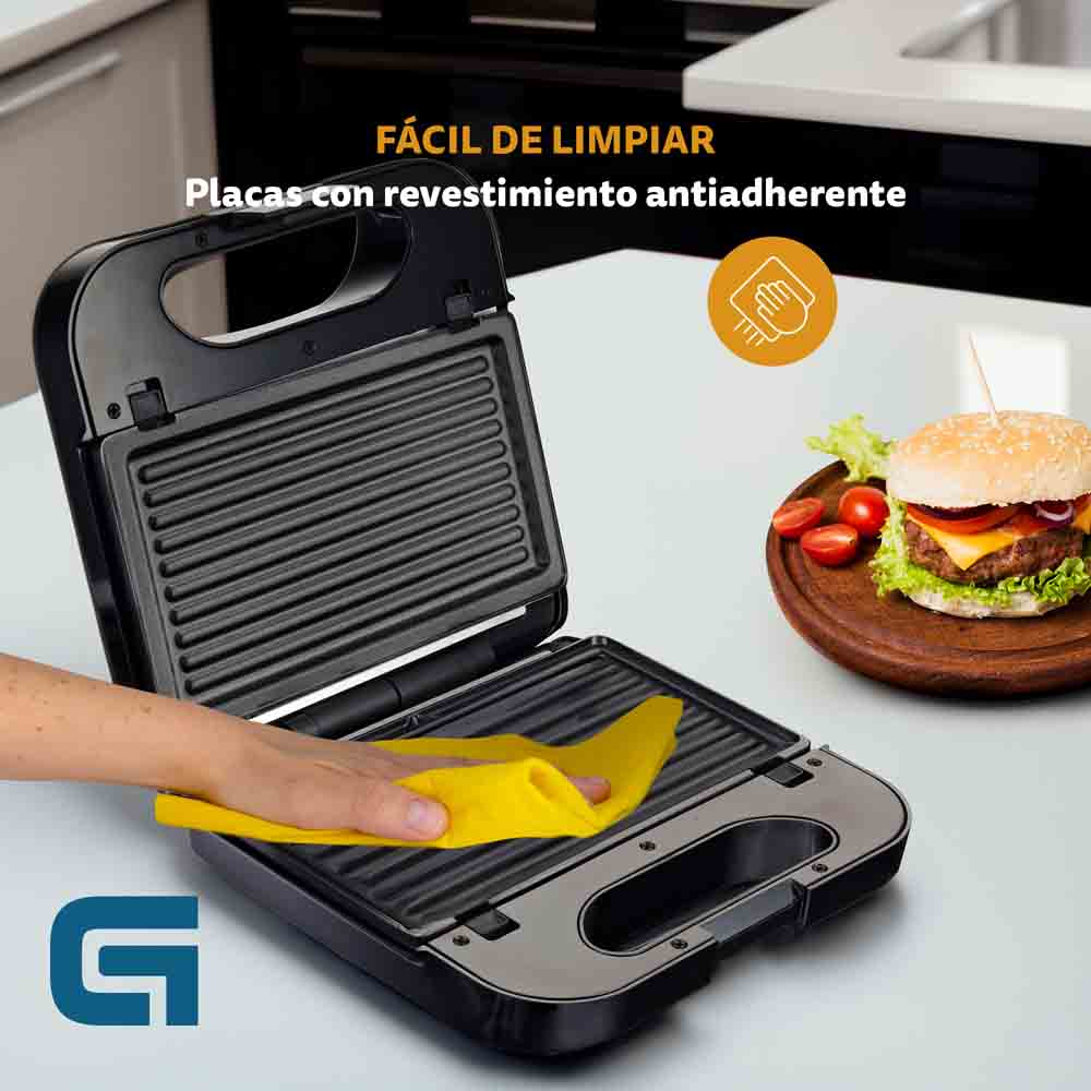 Una macchina per sandwich è aperta, con una mano che tiene un panno giallo e un hamburger a lato.