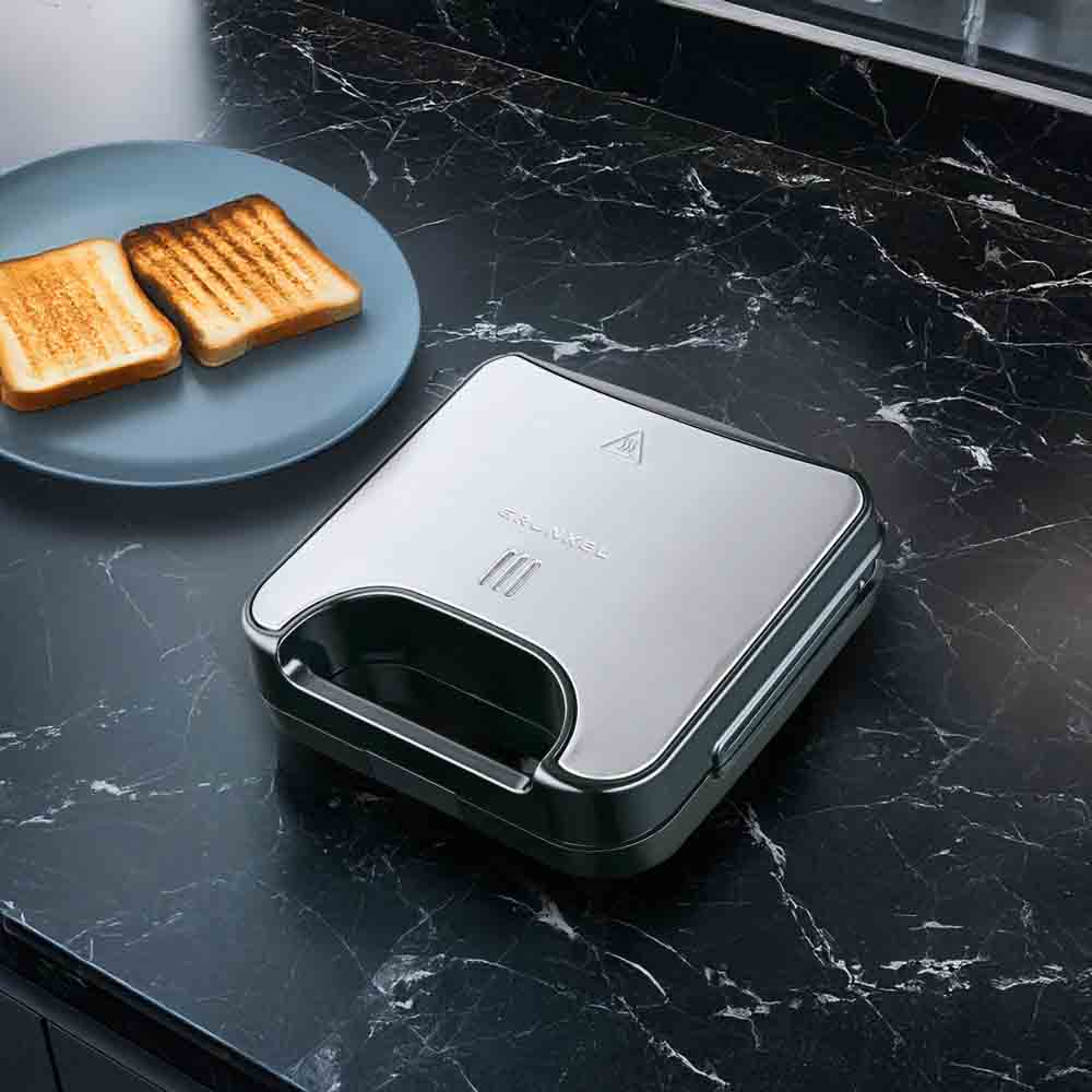 Piastra per sandwich con due sandwich tostati su un piatto. Il dispositivo è su una superficie marmorizzata.