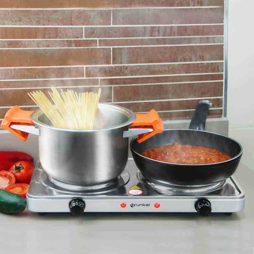 Una estufa eléctrica con una olla de pasta y una sartén con salsa. Tomate y pepino cerca.
