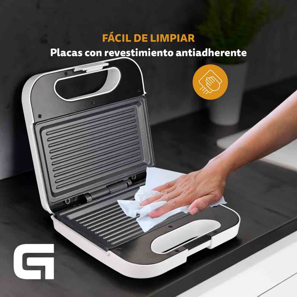 Una sandwichera blanca está abierta. Una mano la limpia con una toalla de papel.