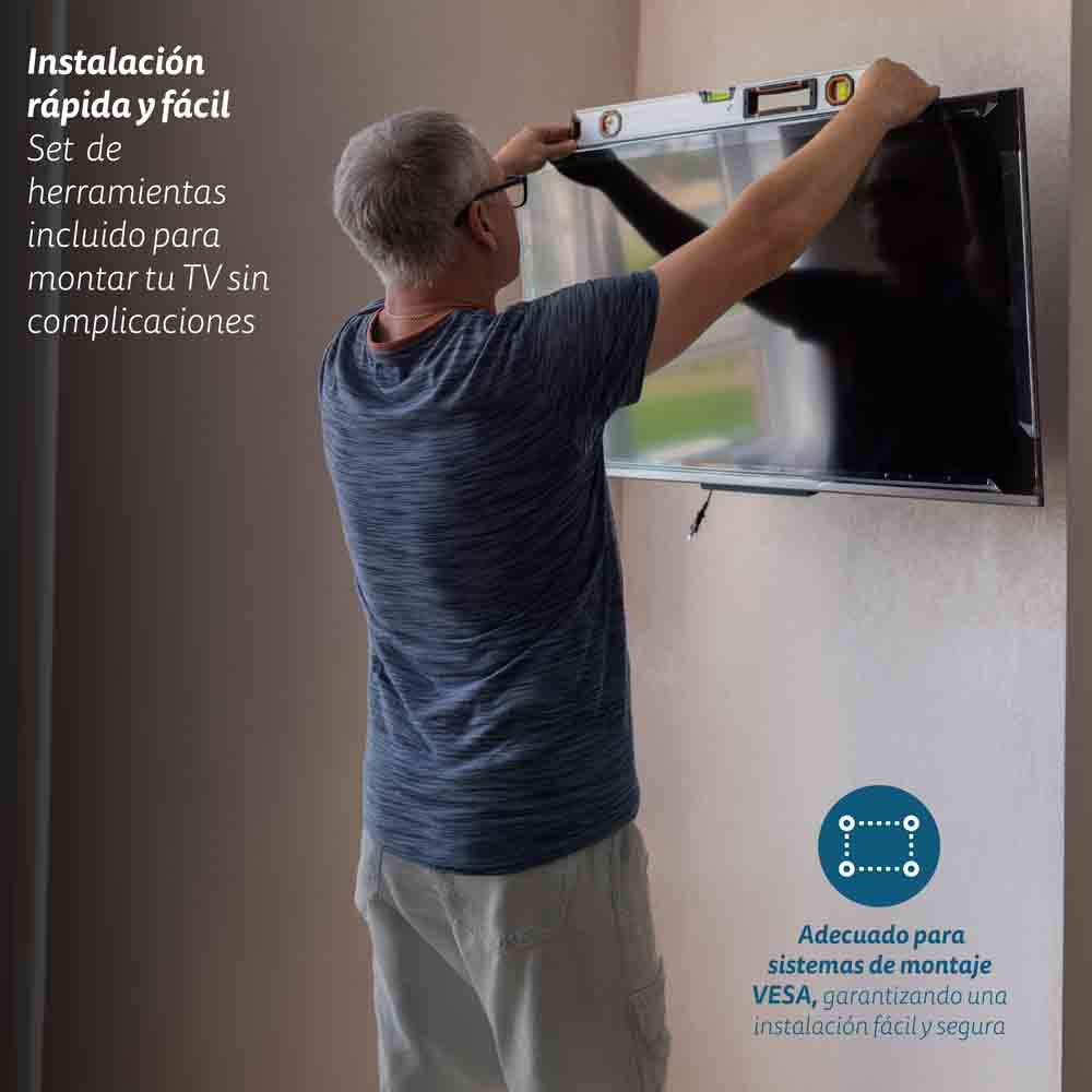 Una persona colgando un televisor en la pared, usando herramientas y un nivel.