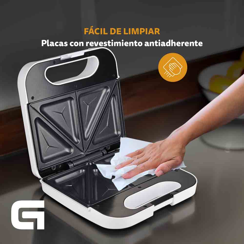 Una sandwichera blanca abierta con una mano limpiando su superficie interior con un paño.