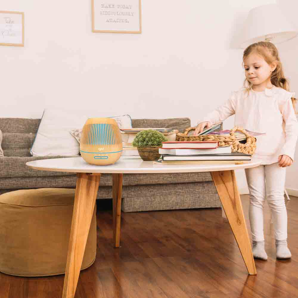 Un bambino è vicino a un tavolo con un diffusore, libri e un cestino in un soggiorno.