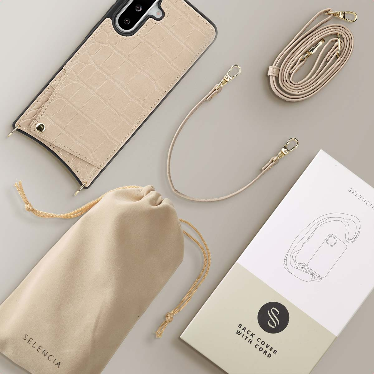 Un étui de téléphone beige avec un motif crocodile est posé à côté d'une sangle assortie et d'un sac à cordon.