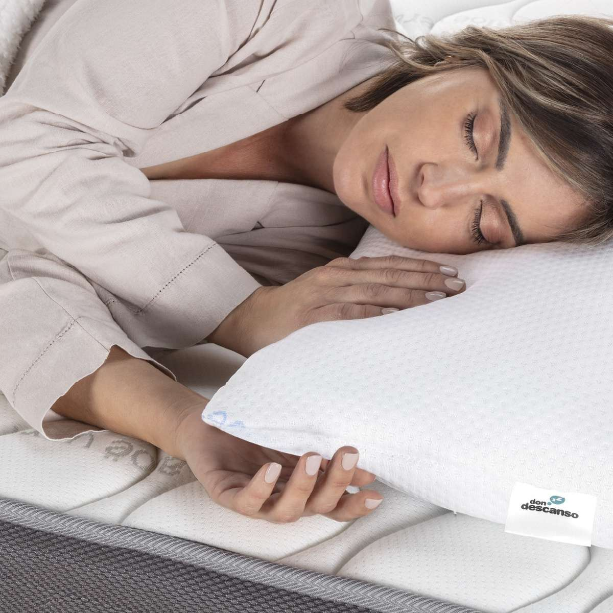 Mujer durmiendo en una almohada blanca sobre un colchón. Lleva una bata beige.