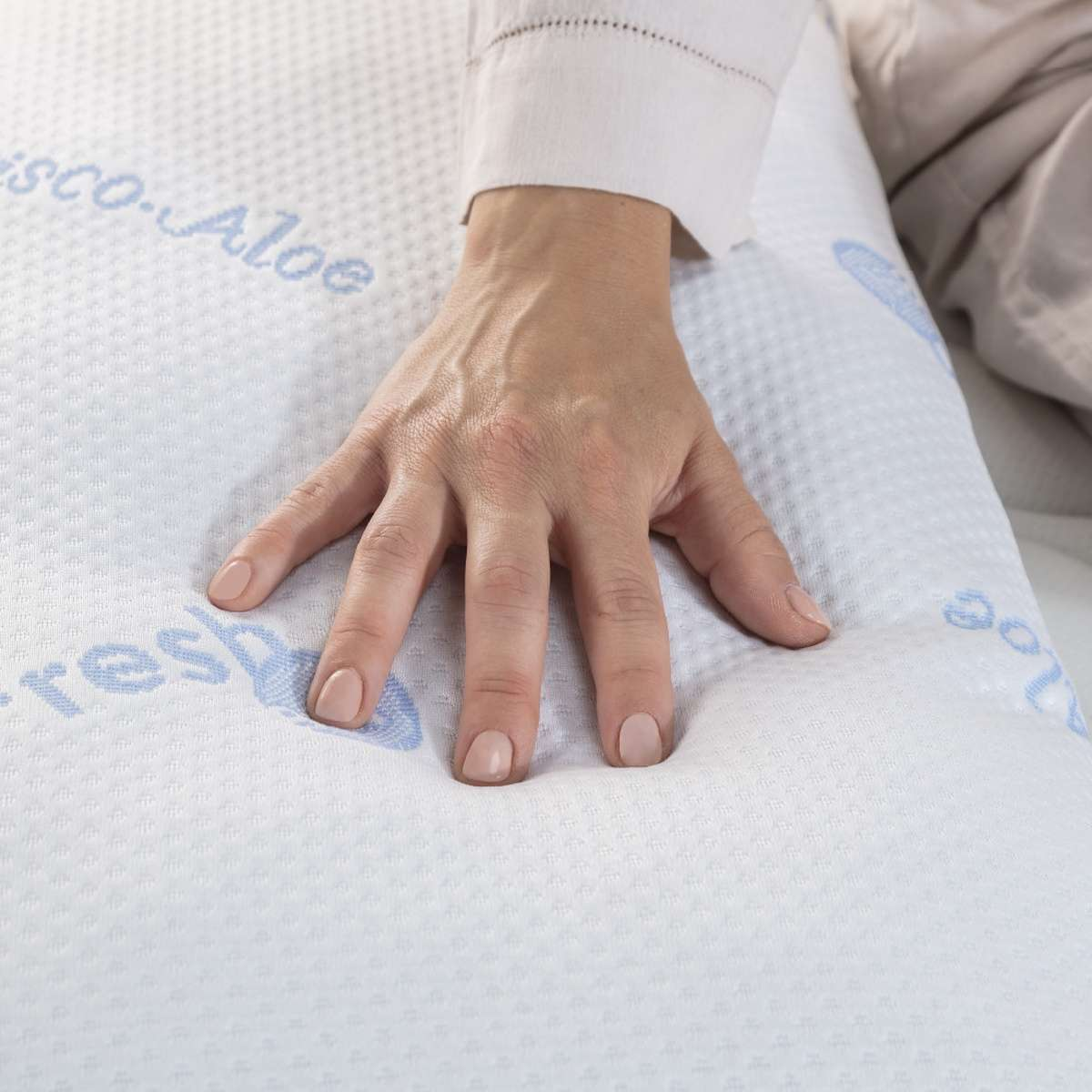 Mano presionando un colchón blanco con texto azul Visco-Aloe.