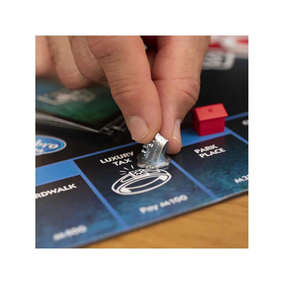 Eine Hand, die ein silbernes Schuhstück auf ein Monopoly-Spielbrett legt.