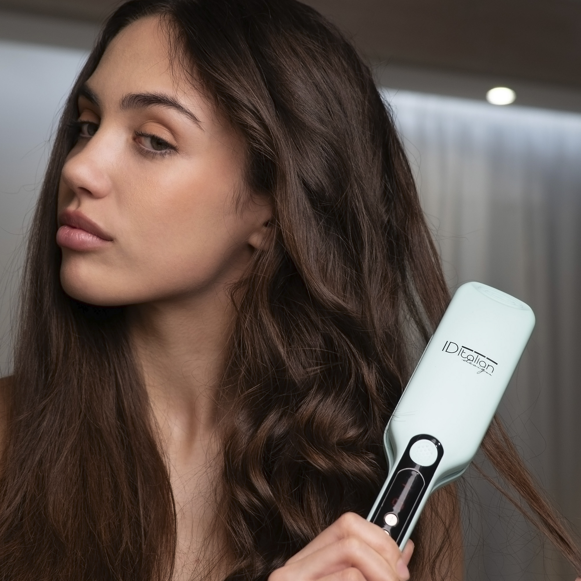 Kobieta z długimi brązowymi włosami używająca turkusowej szczotki do prostowania włosów.