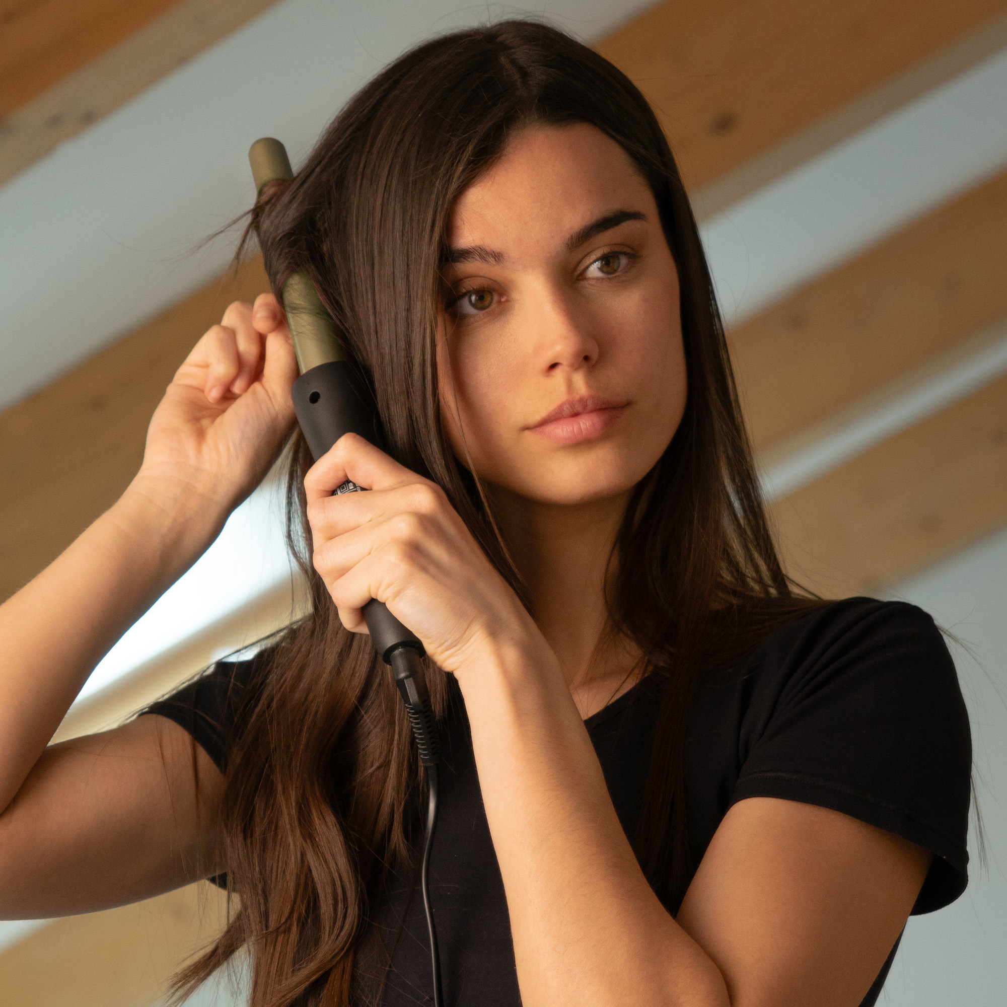 Kobieta kręci włosy lokówką, patrząc w lustro.