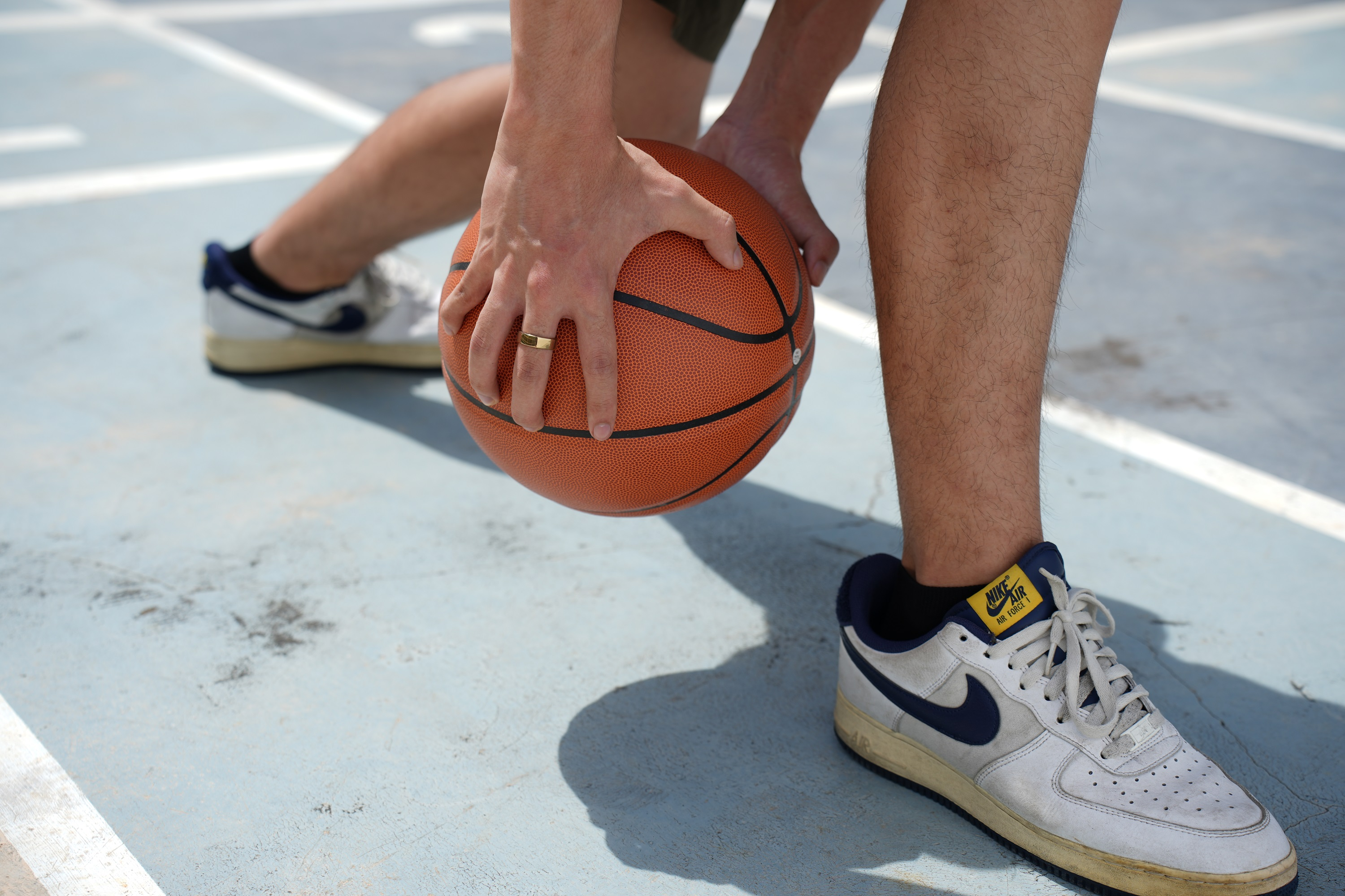 Mann mit Basketball, trägt Nike Air Force 1s. Die Person ist auf einem blauen, Außenplatz.