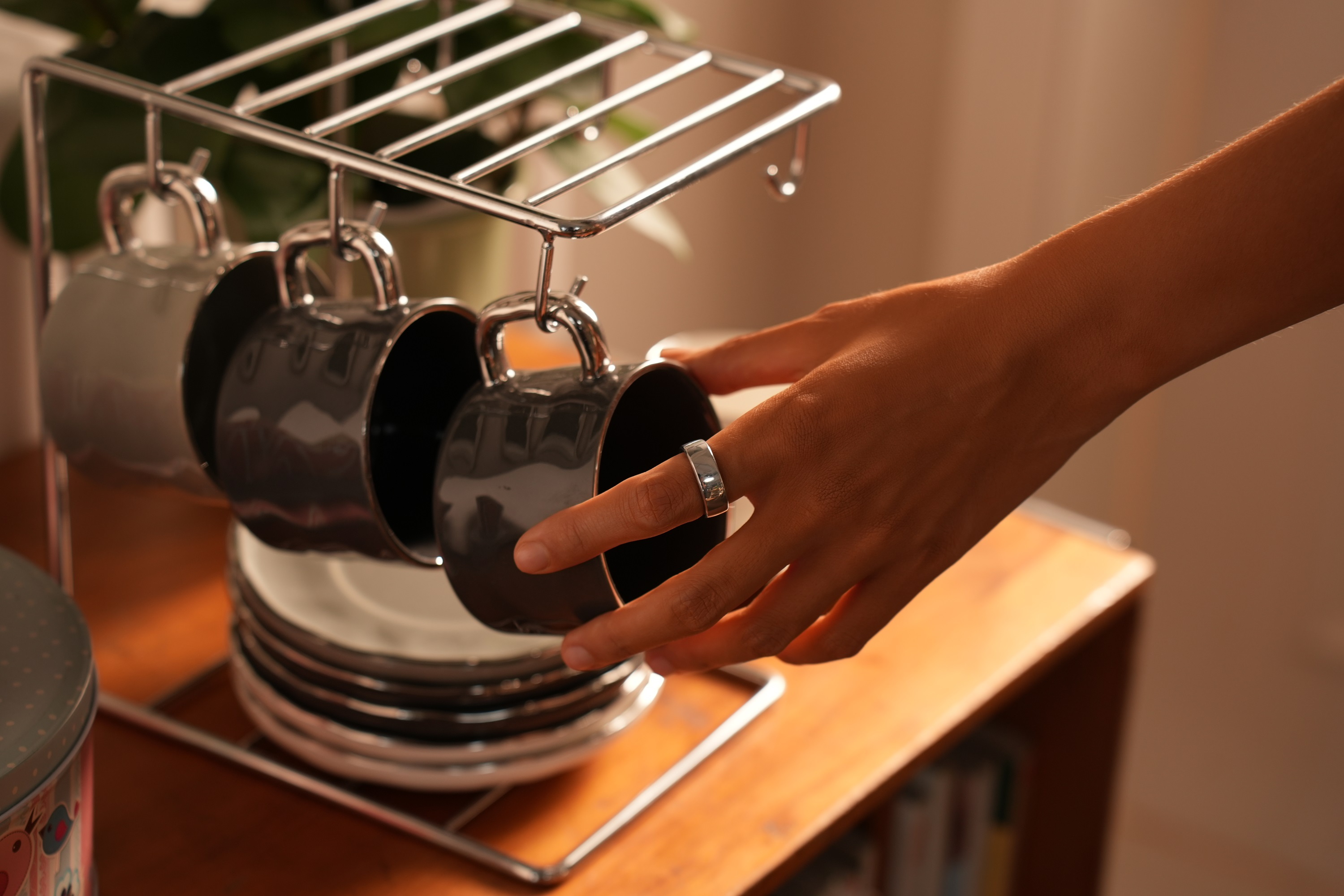 Die Hand einer Person greift nach einer Tasse auf einem Gestell. Am Finger ist ein Ring.