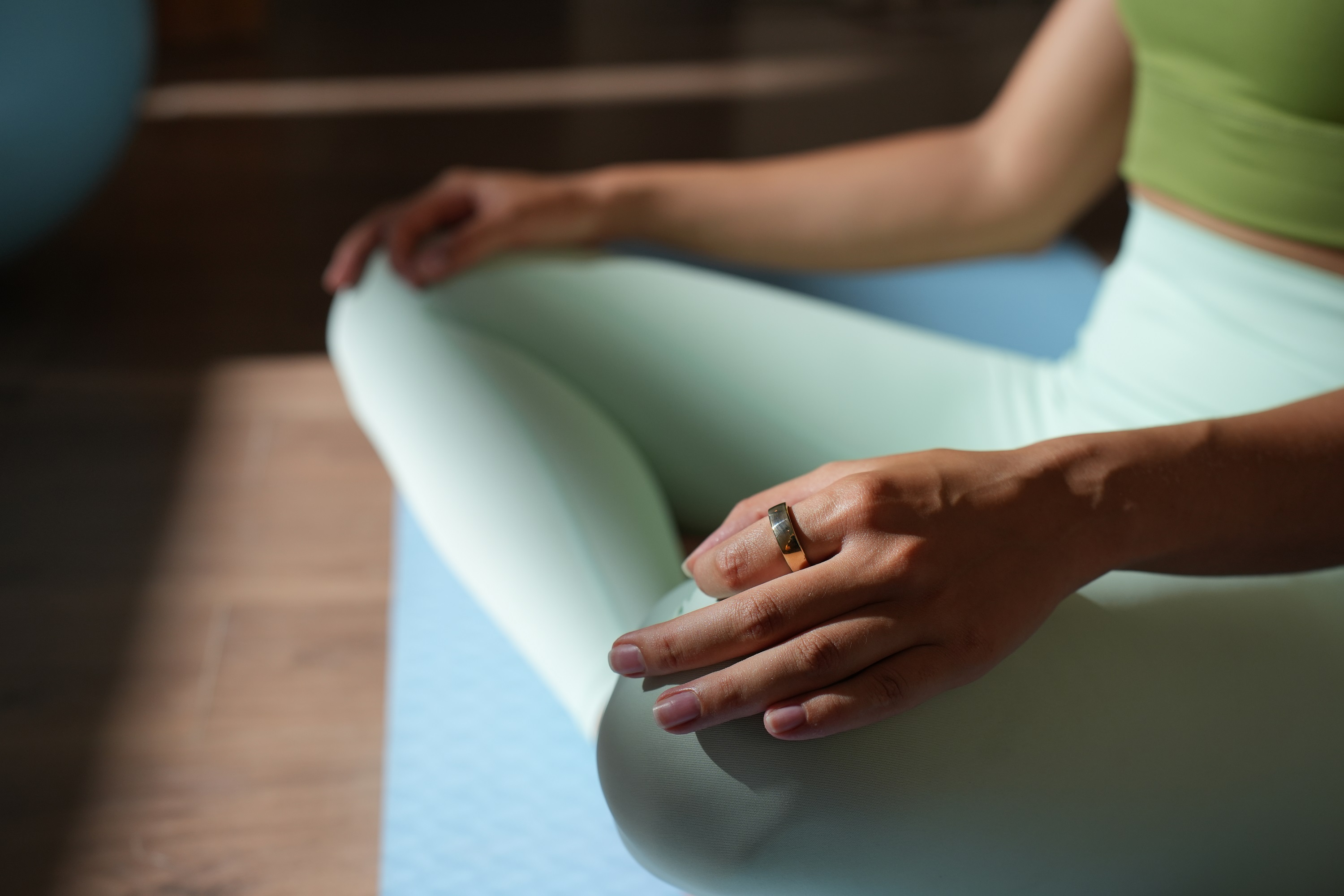 Eine Frau sitzt in einer Yoga-Pose, trägt Grün und hält ihre rechte Hand auf ihrem linken Knie.