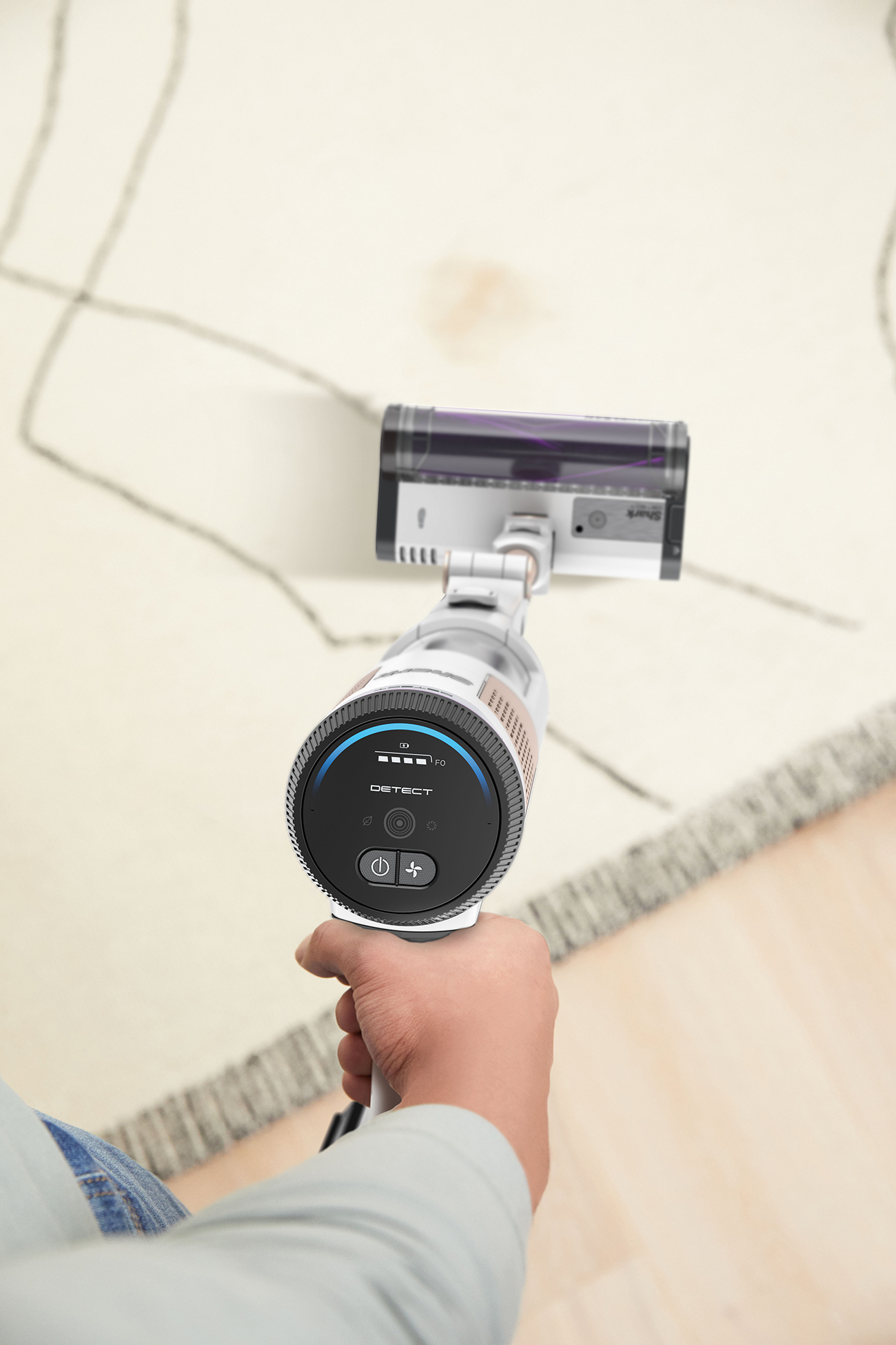 A person holding a vacuum cleaner over a carpet, hand in foreground, vacuum in background.