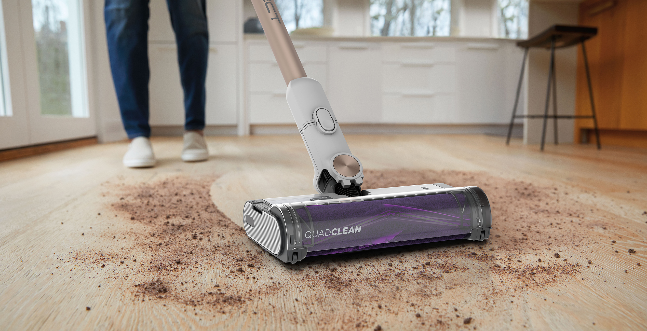 Person vacuuming a wooden floor with a QuadClean vacuum cleaner, indoors, close up.
