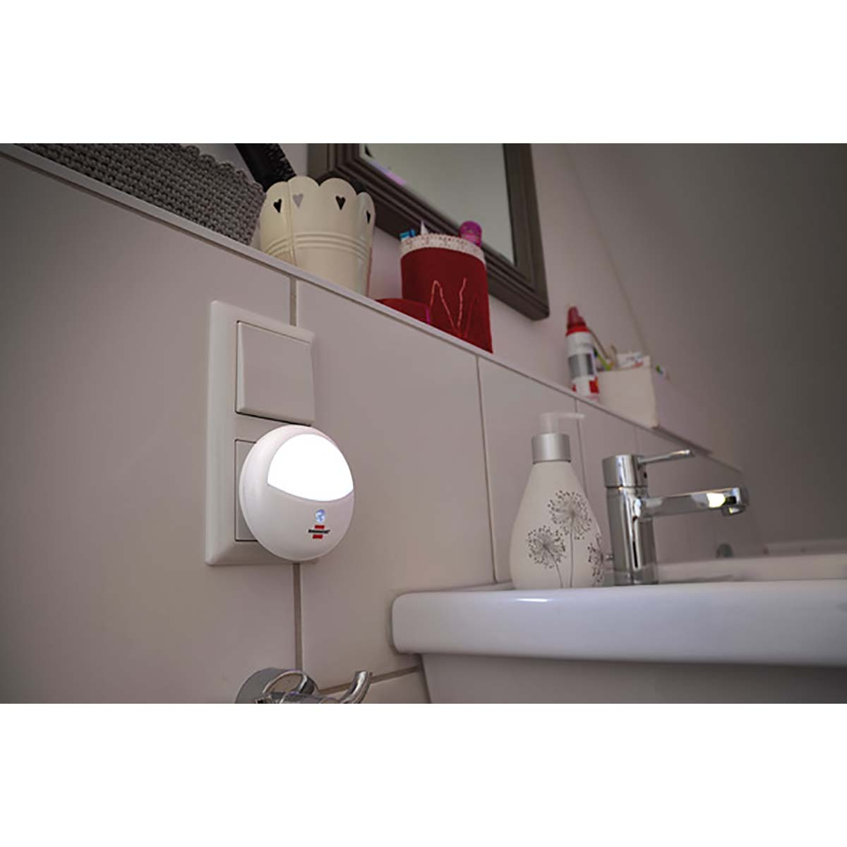 A wall-mounted night light illuminates a bathroom wall and sink. Other items are on the wall.