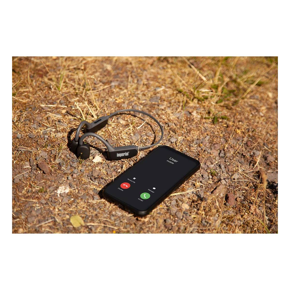 Słuchawki przewodnictwa kostnego i smartfon z ekranem połączenia na trawie.