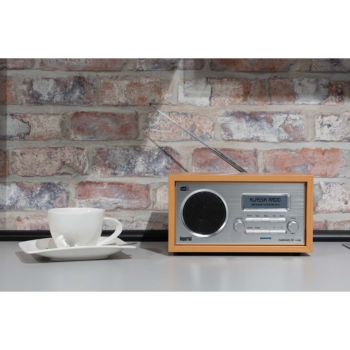 Een radio op een tafel, een kop koffie en een bakstenen muur op de achtergrond.