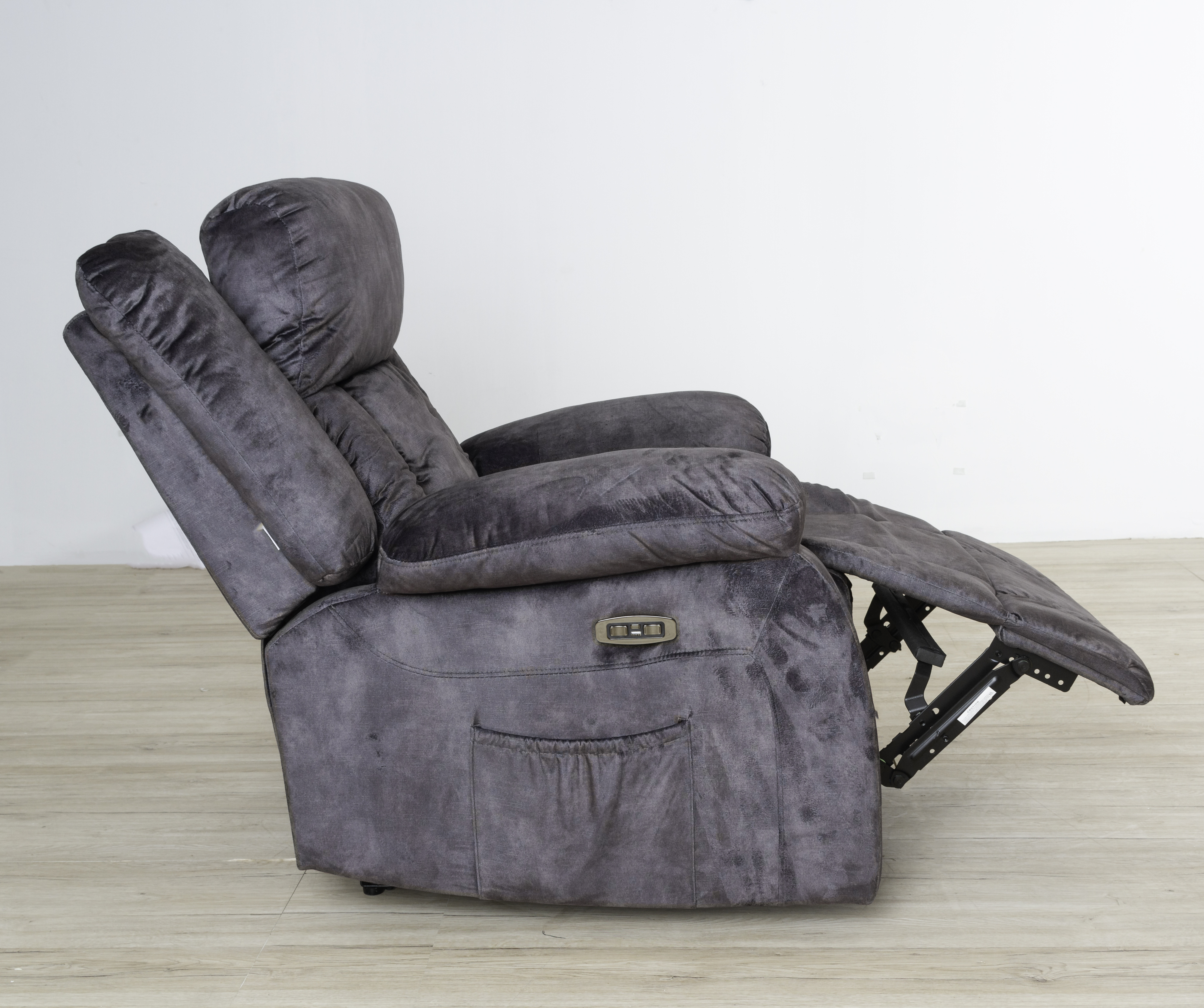 Una silla reclinable gris en posición reclinada. El reposapiés está extendido, mostrando una pared blanca.