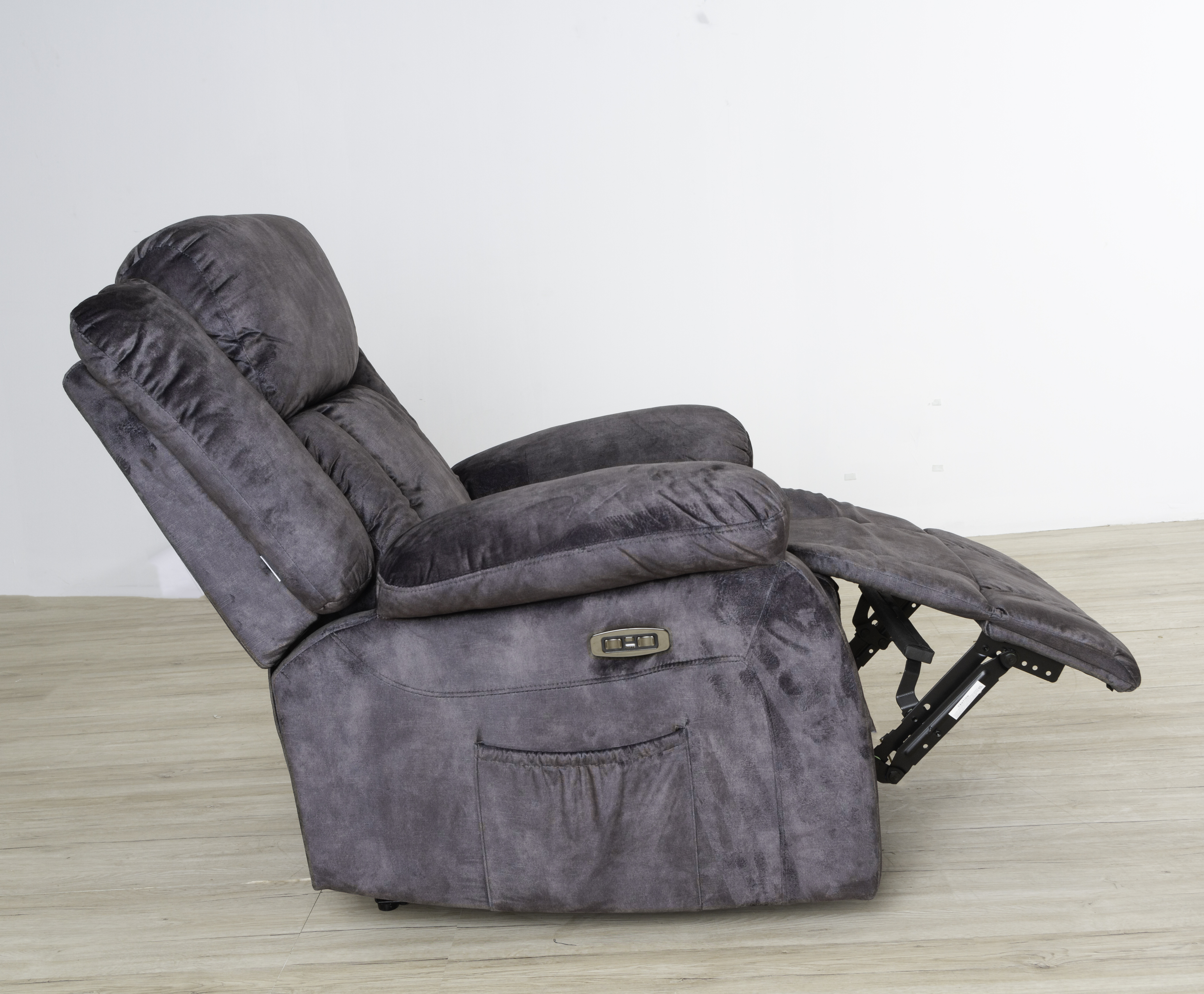 Un sillón reclinable gris con reposapiés extendido. Está sobre un suelo de madera clara contra una pared blanca.
