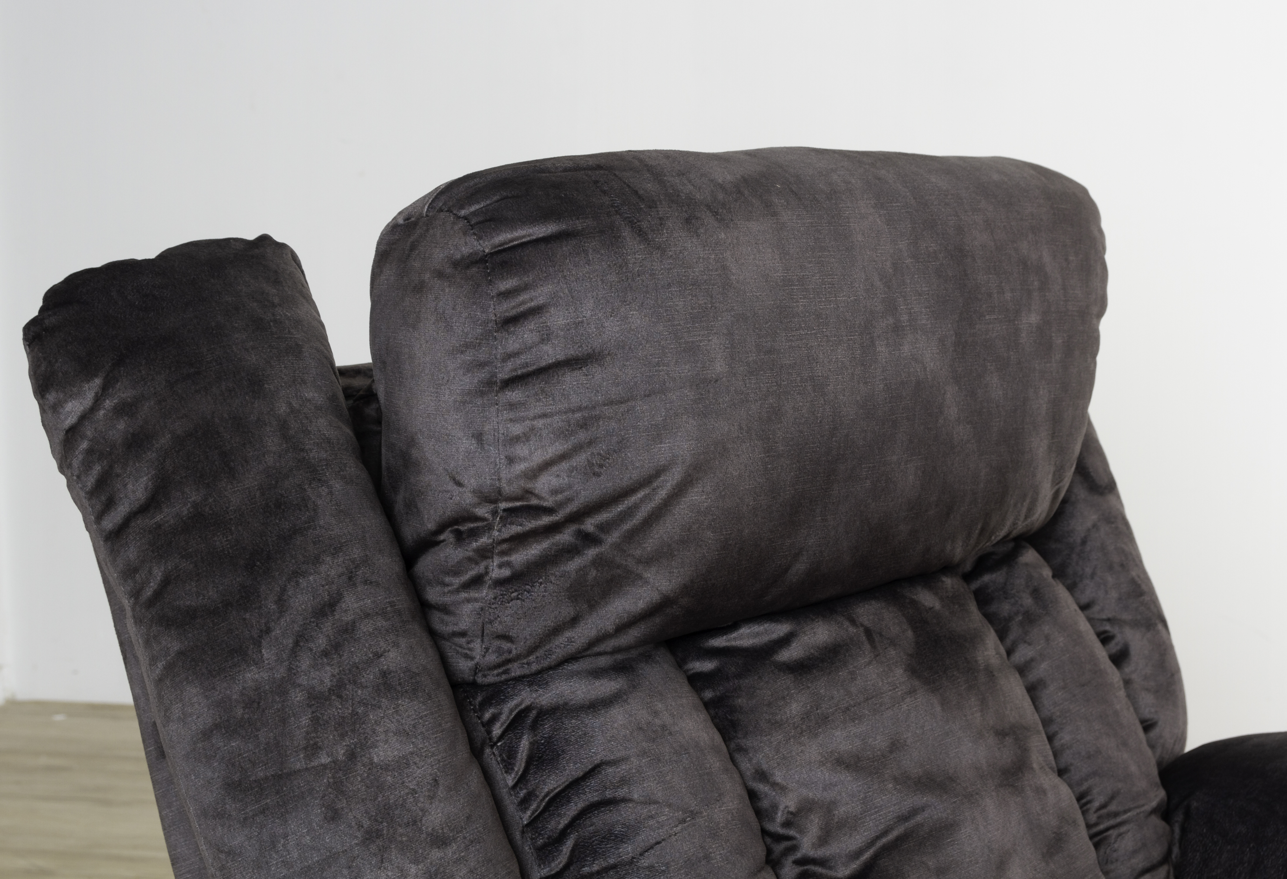 Primer plano del reposacabezas de un sillón reclinable marrón oscuro. El fondo es una pared blanca y un suelo de madera.