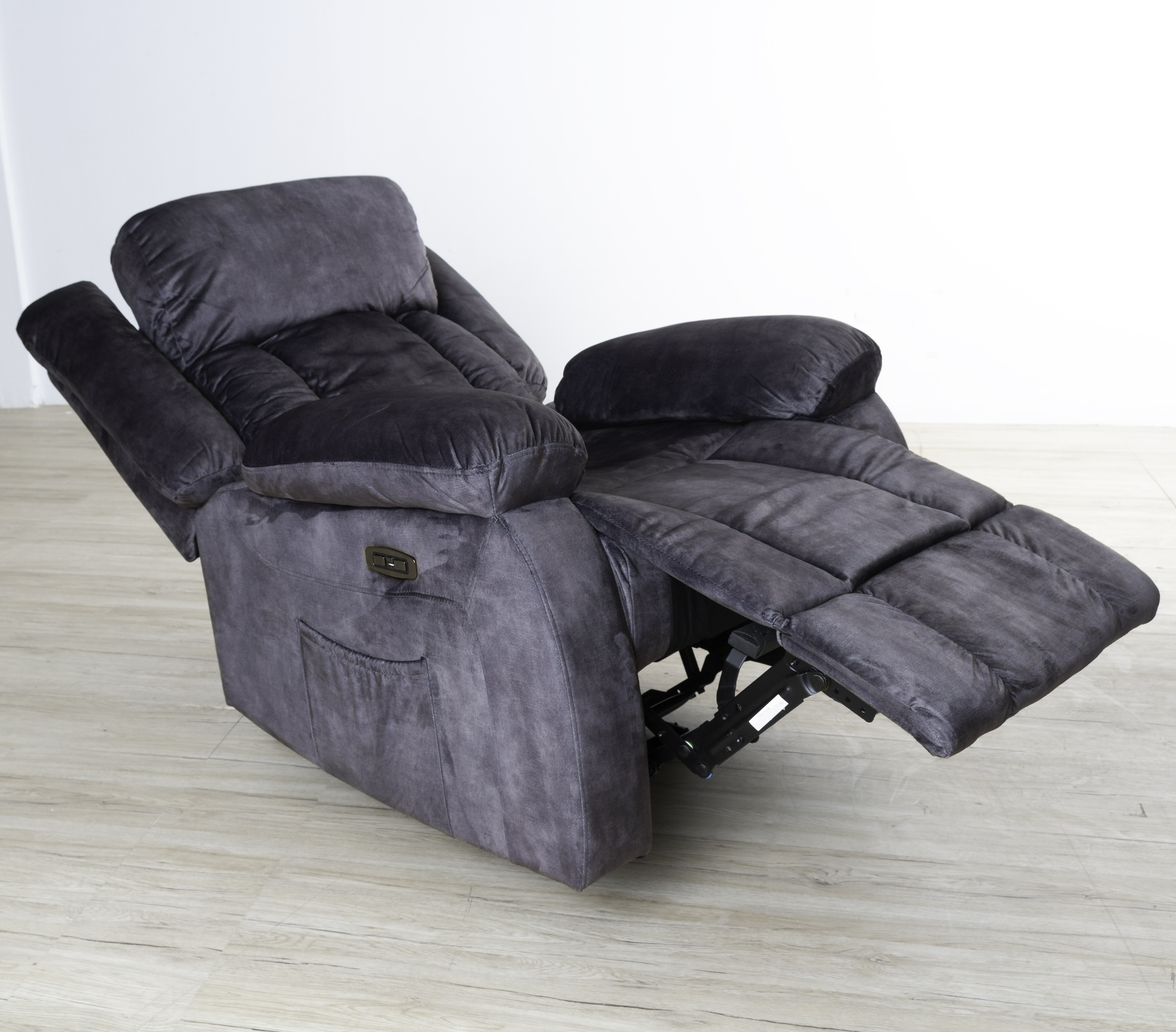 Se muestra un sillón reclinable gris, con el reposapiés extendido. La silla está sobre un piso de madera clara.