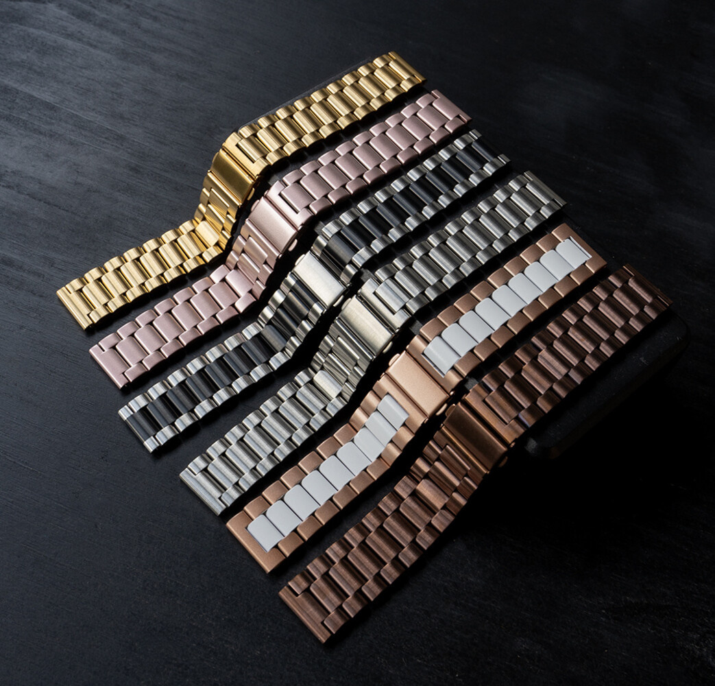 Verschiedene Metalluhrenarmbänder in Gold-, Roségold-, Silber- und Schwarzfarben, auf dunkler Oberfläche.