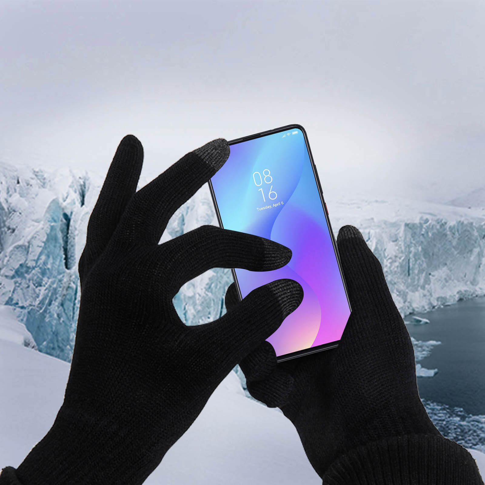 Mani con guanti neri toccano lo schermo di un telefono, con un paesaggio innevato sullo sfondo.