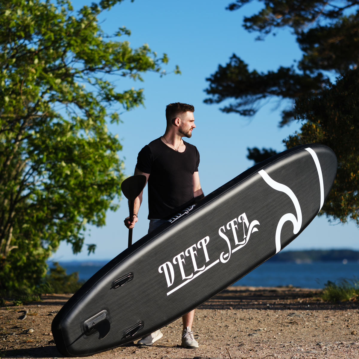 Mężczyzna trzymający czarną deskę do wiosłowania na stojąco z białym tekstem na plaży.