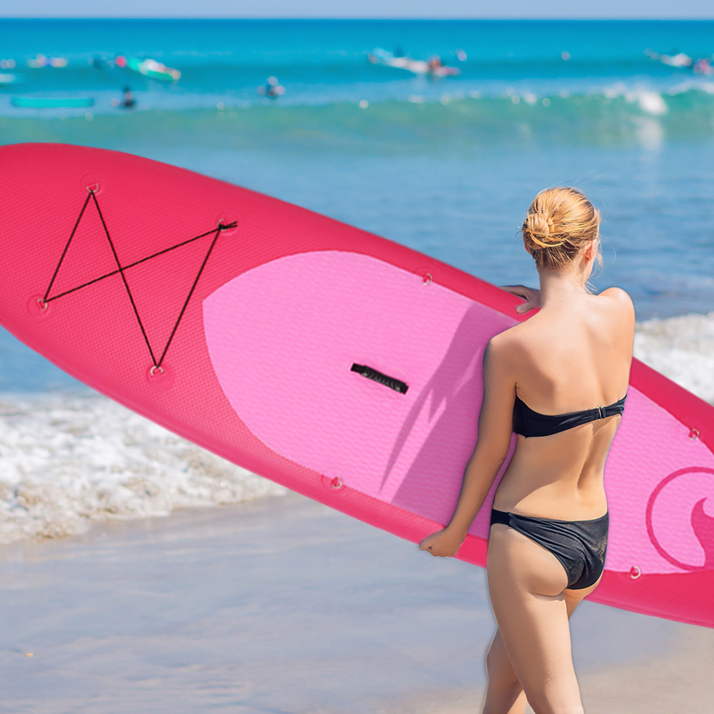 Kobieta trzyma różowo-czerwoną deskę do wiosłowania na plaży, tyłem do morza, w bikini.