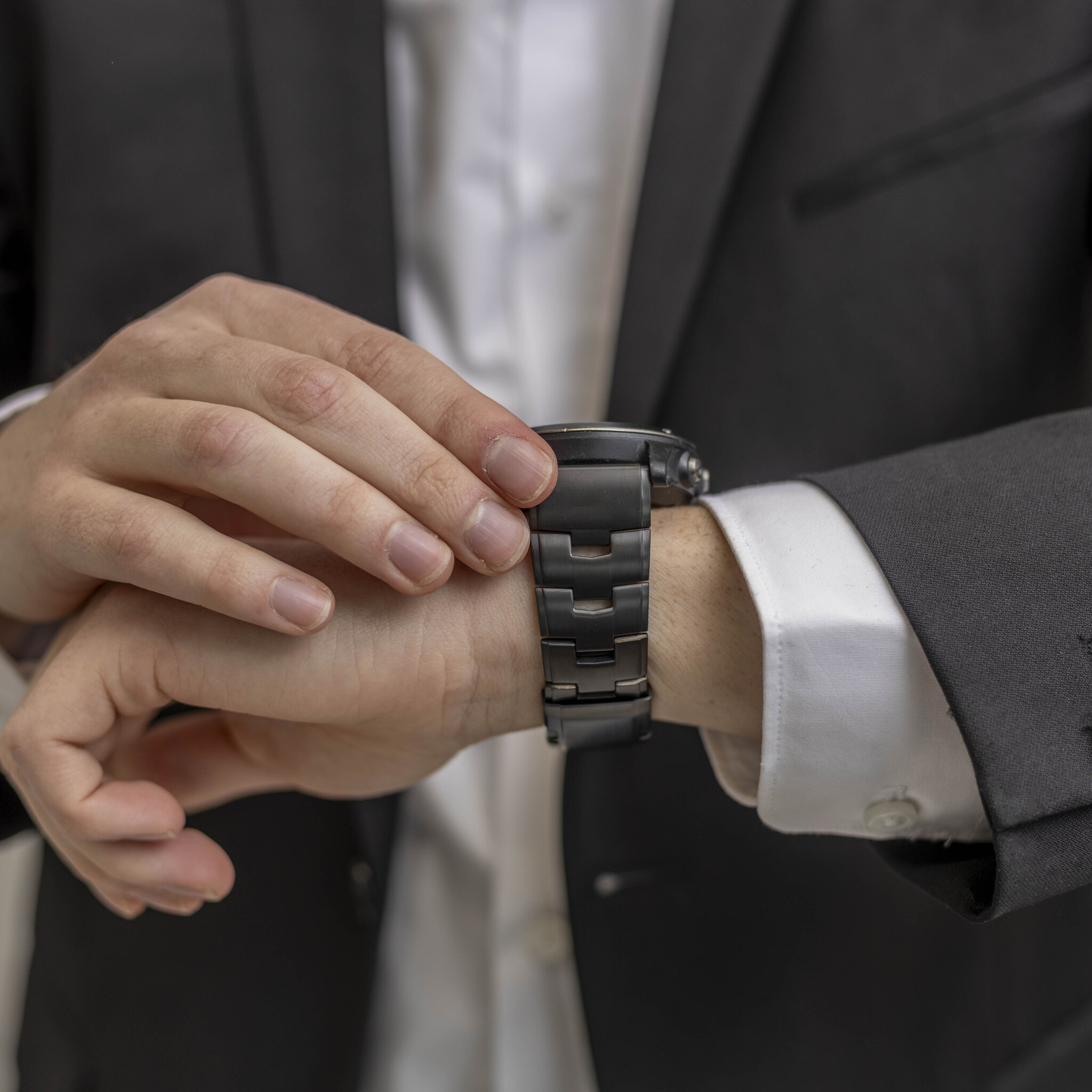 Ein Mann im Anzug betrachtet seine schwarze Uhr.