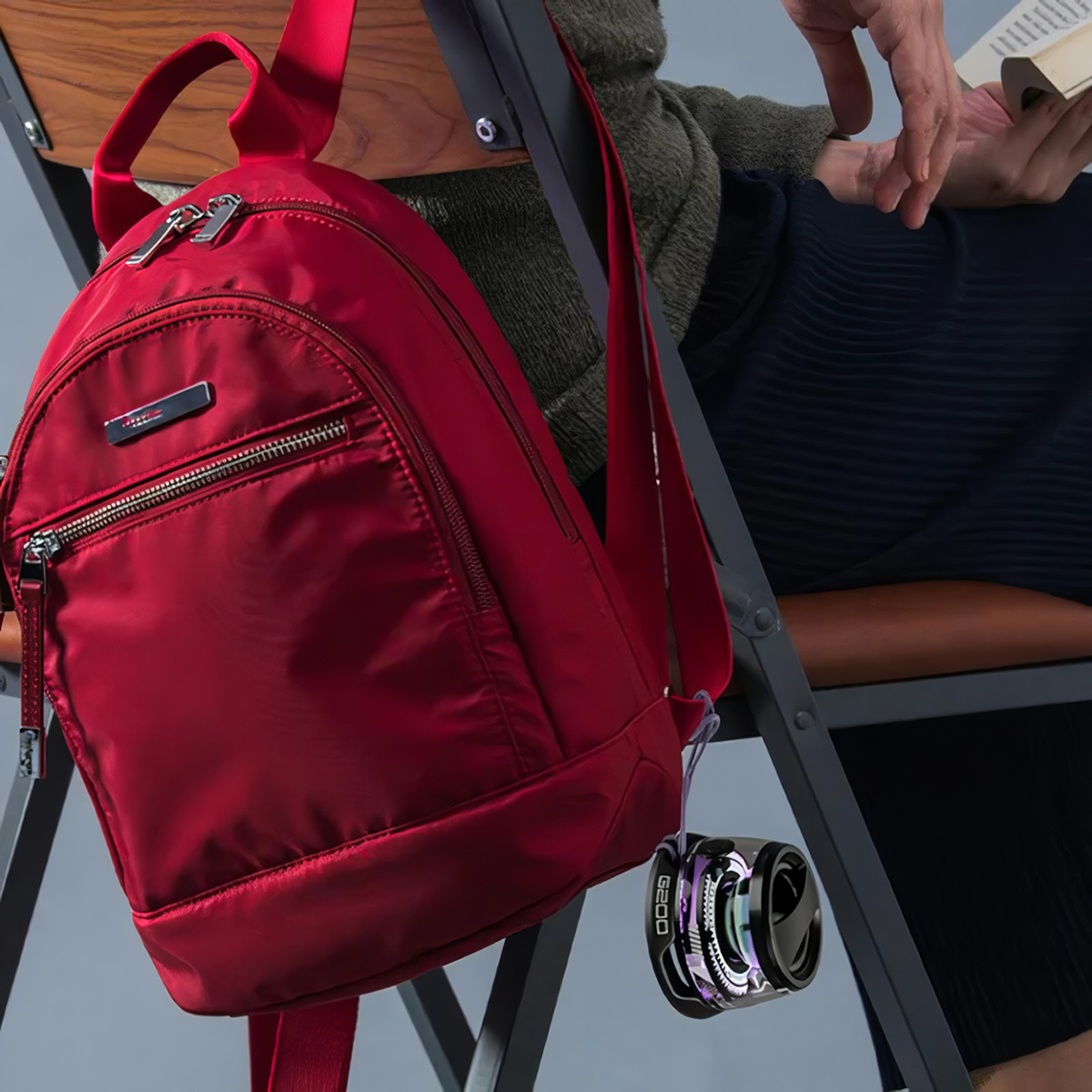 Una mochila roja cuelga de una silla. Una persona está sentada cerca sosteniendo un libro.