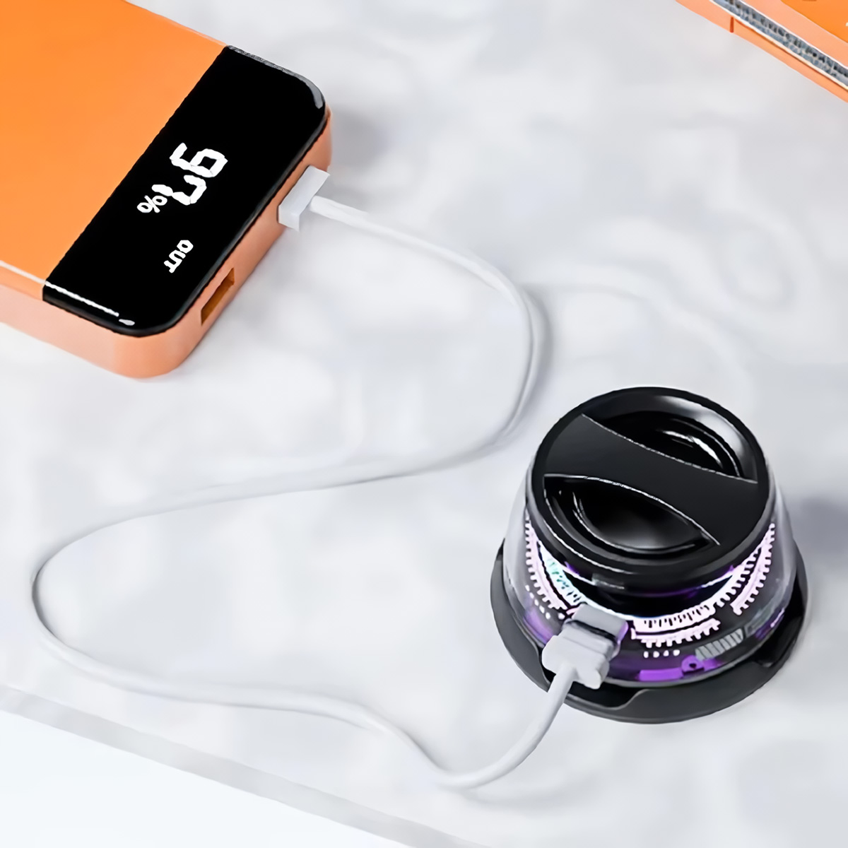 Banco de energía naranja cargando un dispositivo negro y morado. Un cable blanco conecta los dispositivos.