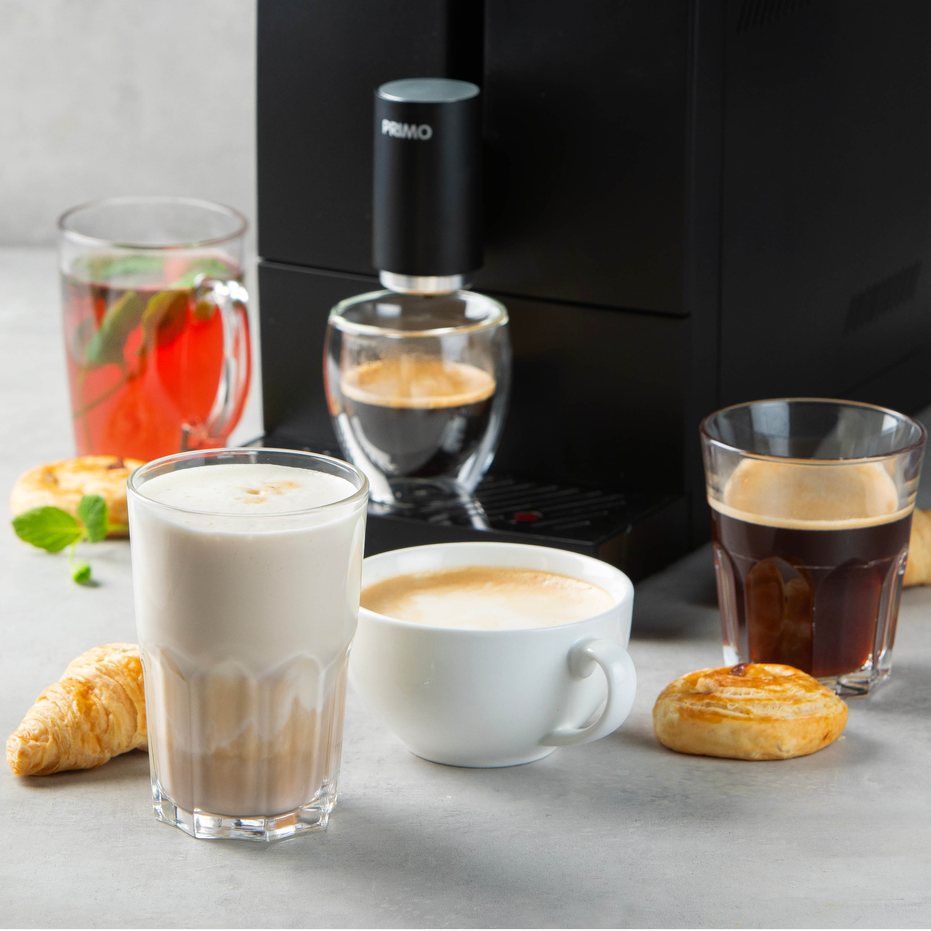 Machine à café avec diverses boissons : latte, café, thé. Croissant, pâtisserie et menthe. Fond clair.