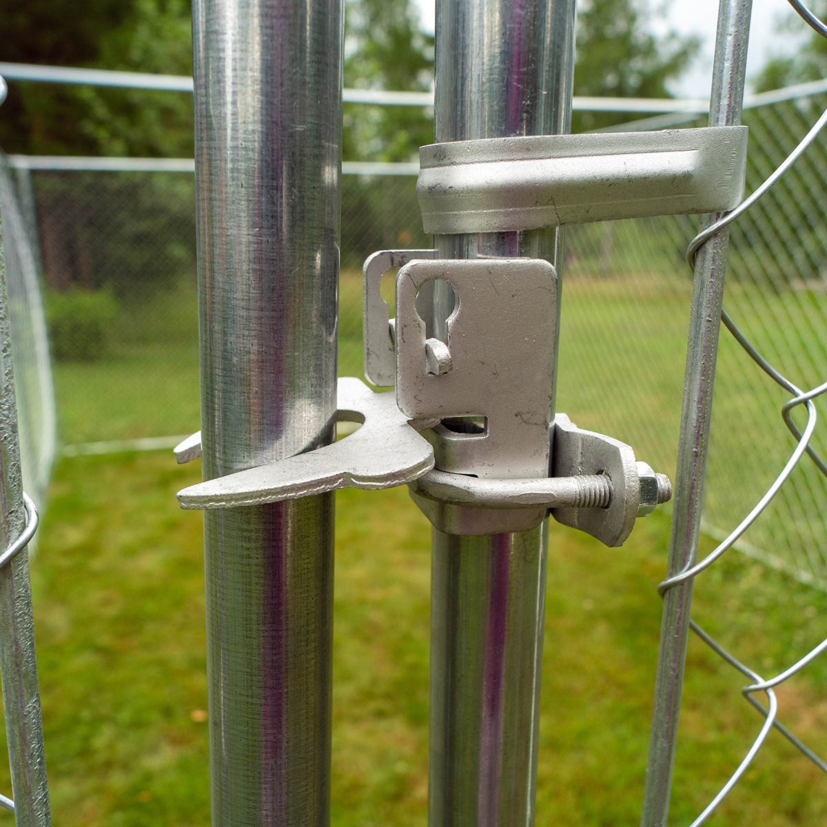 Ein Metalltorverschluss an einem Maschendrahtzaun. Silberne Hardware vor grünem Gras.