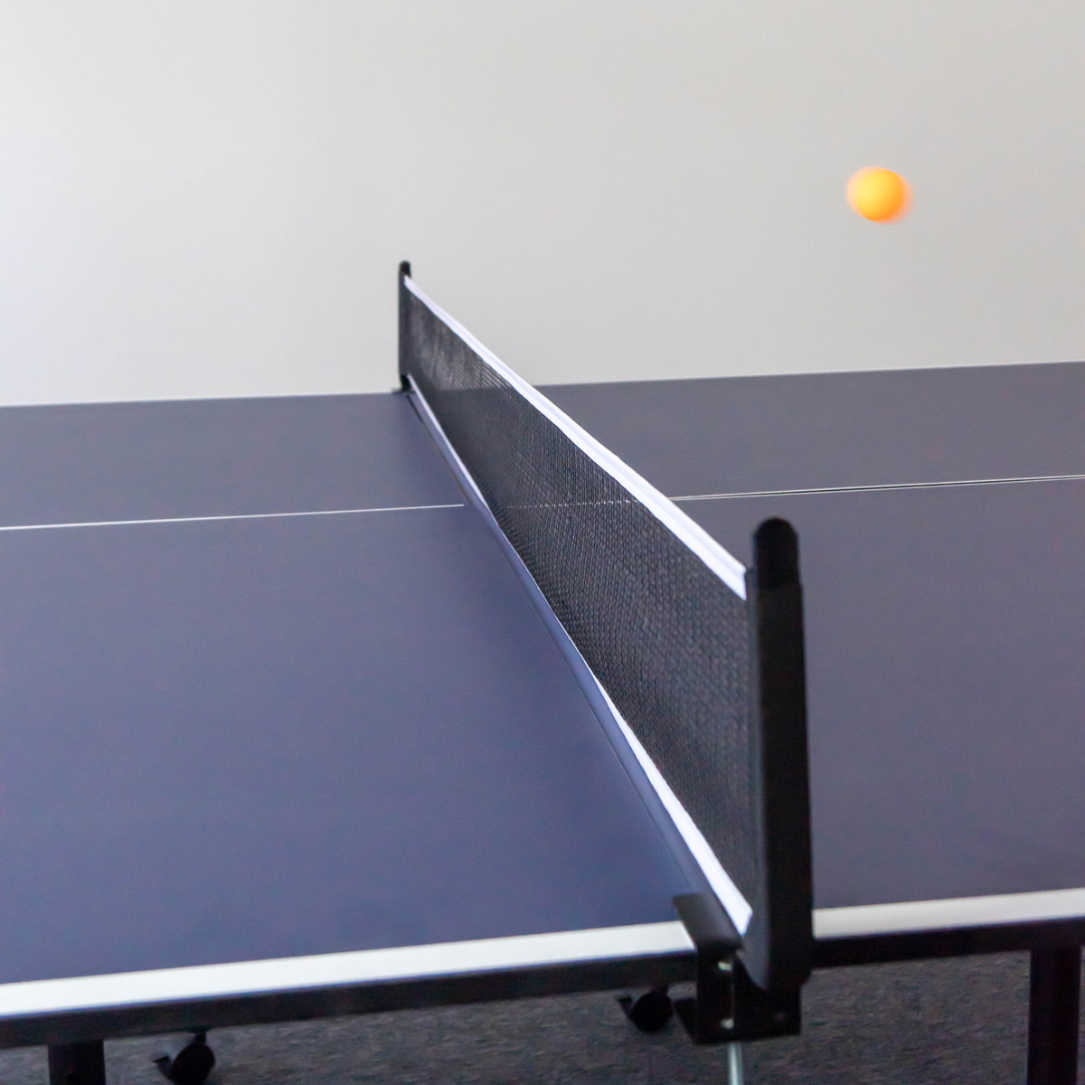 Eine Tischtennisplatte mit Netz und ein Tischtennisball in der Luft.