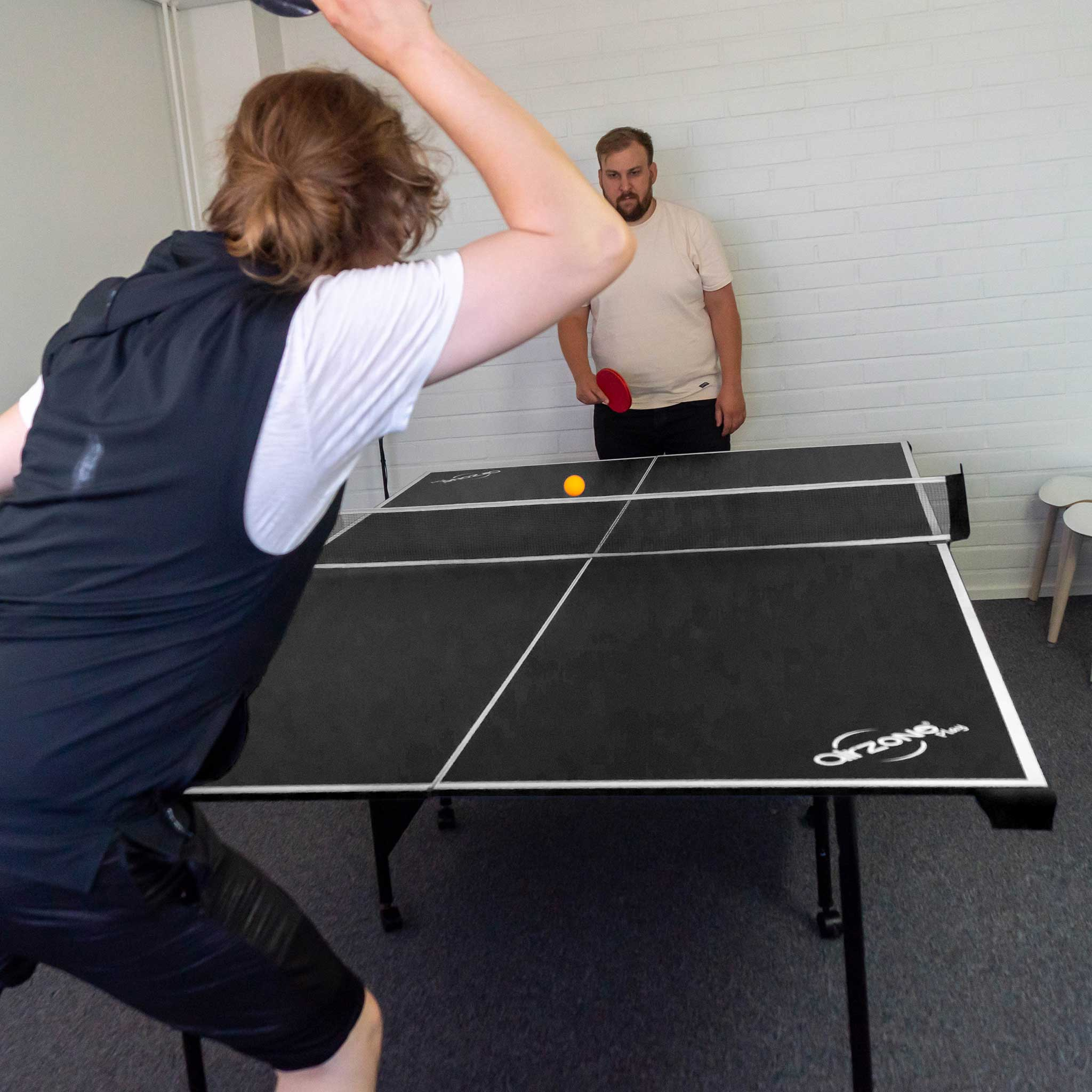 Zwei Personen spielen Tischtennis. Ein gelber Ball liegt auf dem Tisch. Einer schlägt ihn gleich.
