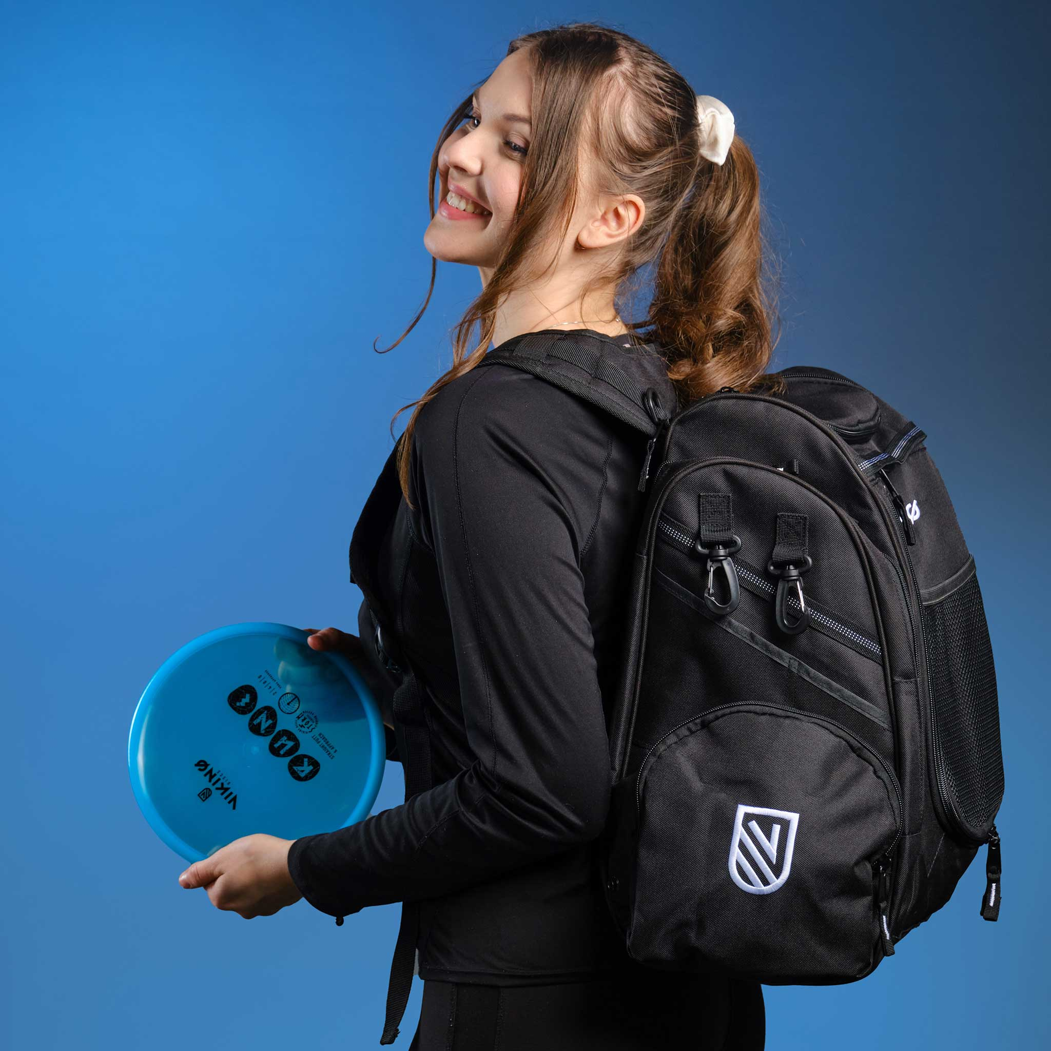 Frau mit Rucksack hält blaue Scheibe, lächelt nach links.