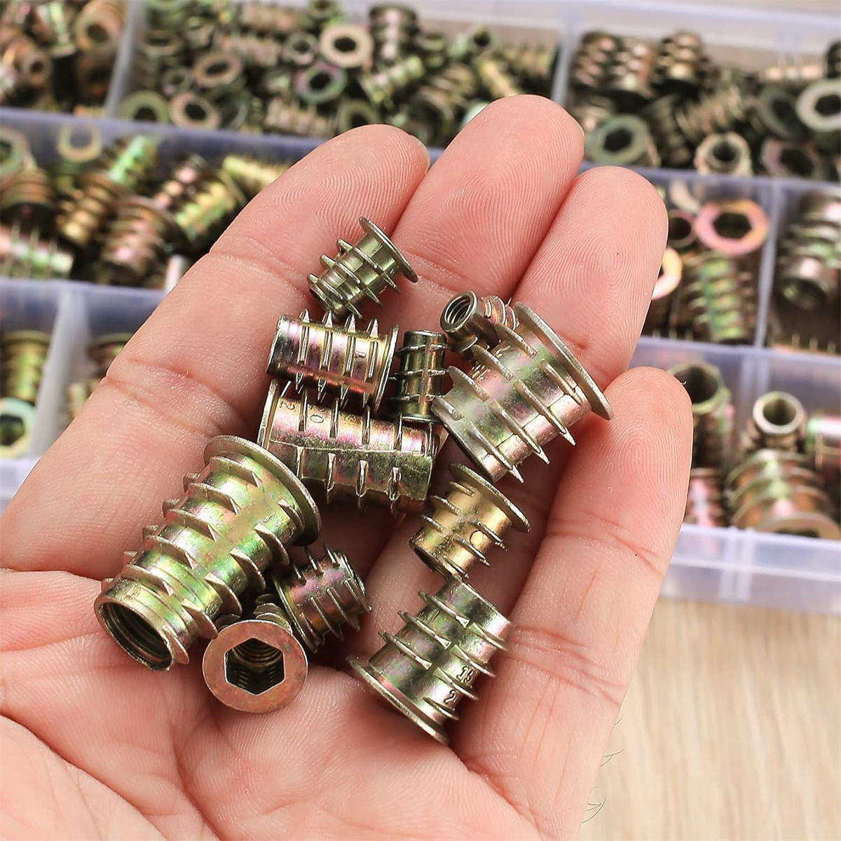 Eine Hand, die eine Sammlung von Gewindeeinsätzen aus Metall hält, umgeben von anderen.