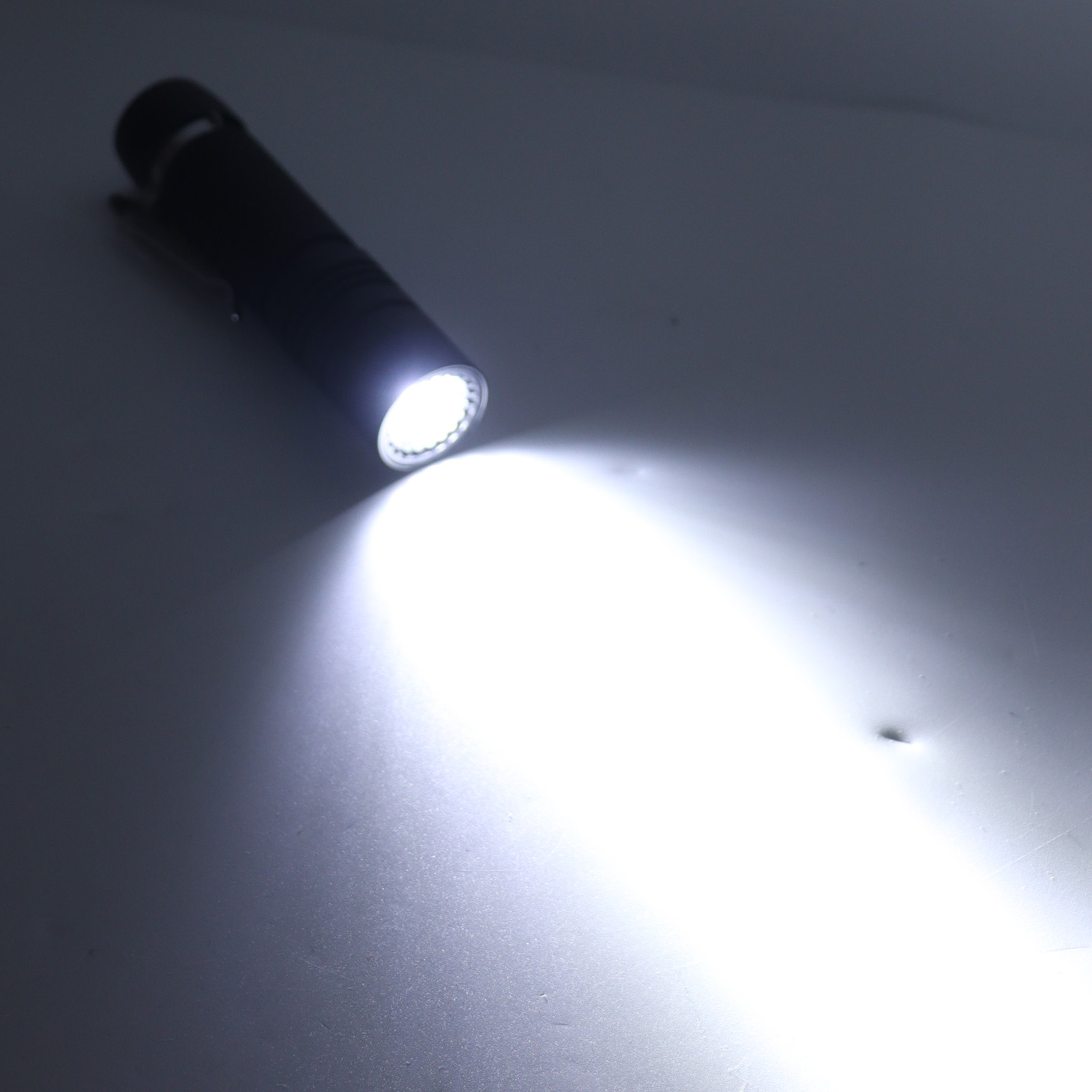 Eine schwarze Taschenlampe, die einen hellen, fokussierten Lichtstrahl auf eine weiße Oberfläche aussendet.